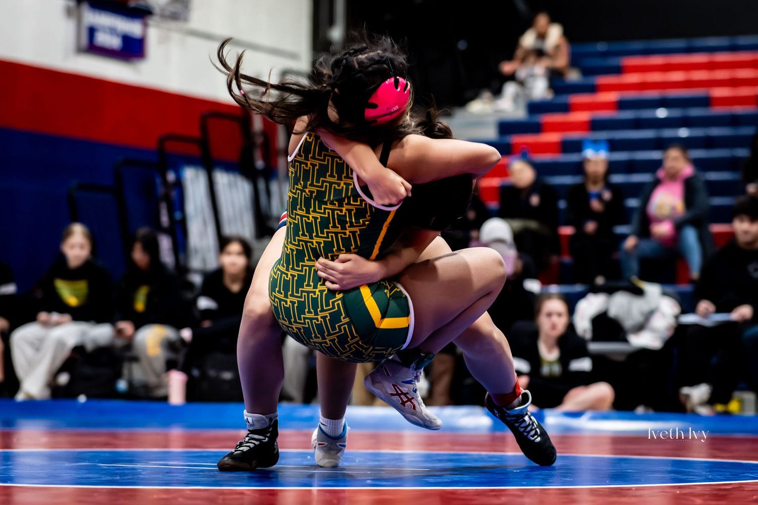 Two wrestlers compete in a high school match on a blue wrestling mat during an intense competition.