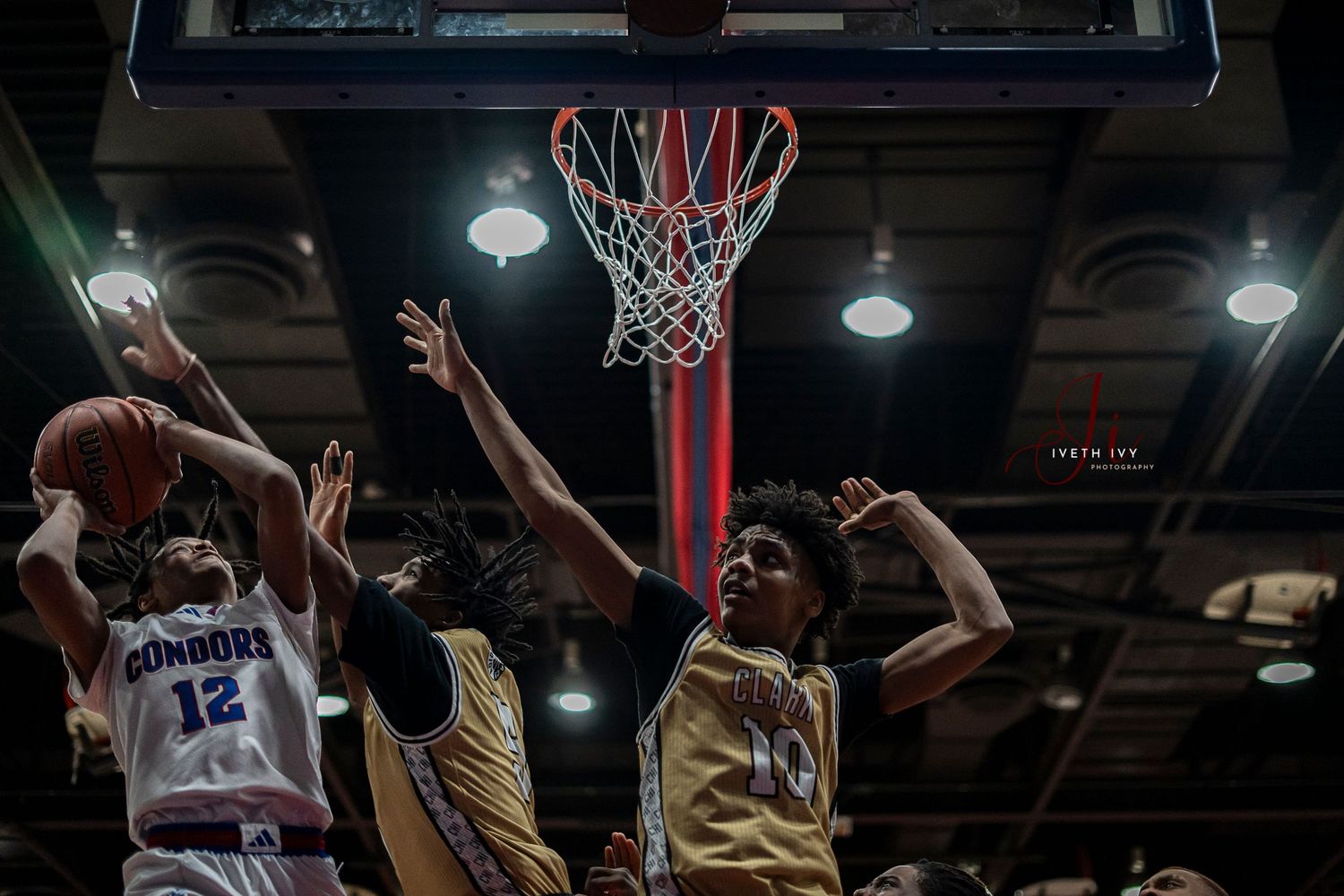 Basketball player rises up for a slam dunk attempt during an intense game with defenders trying to block.