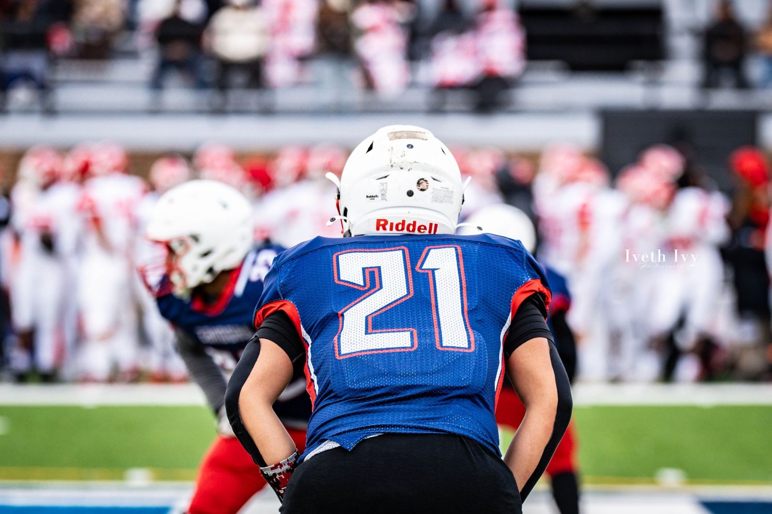 Football players in blue and red uniforms line up on the field during a competitive game.