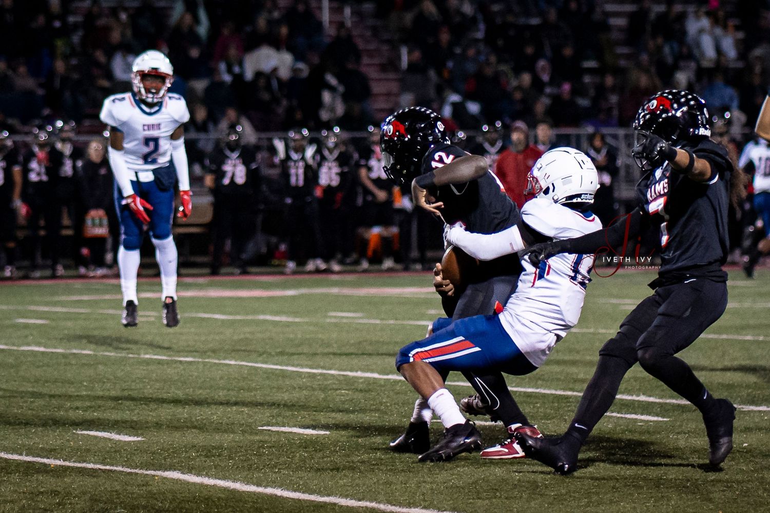 Players compete during a nighttime football game under stadium lights on a dark field with players in white and red uniforms.