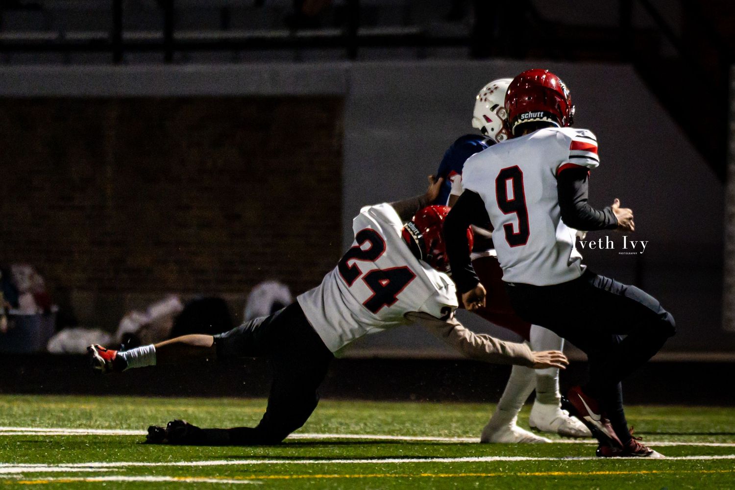 Football players collide in a tackle during an intense game at night under stadium lights.