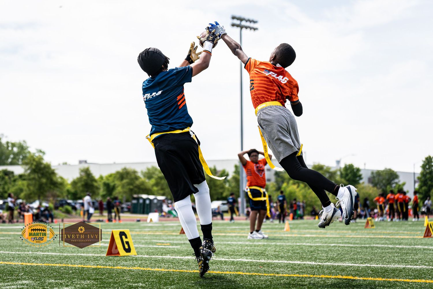 Two flag football players leap to contest a pass during an outdoor flag football game.