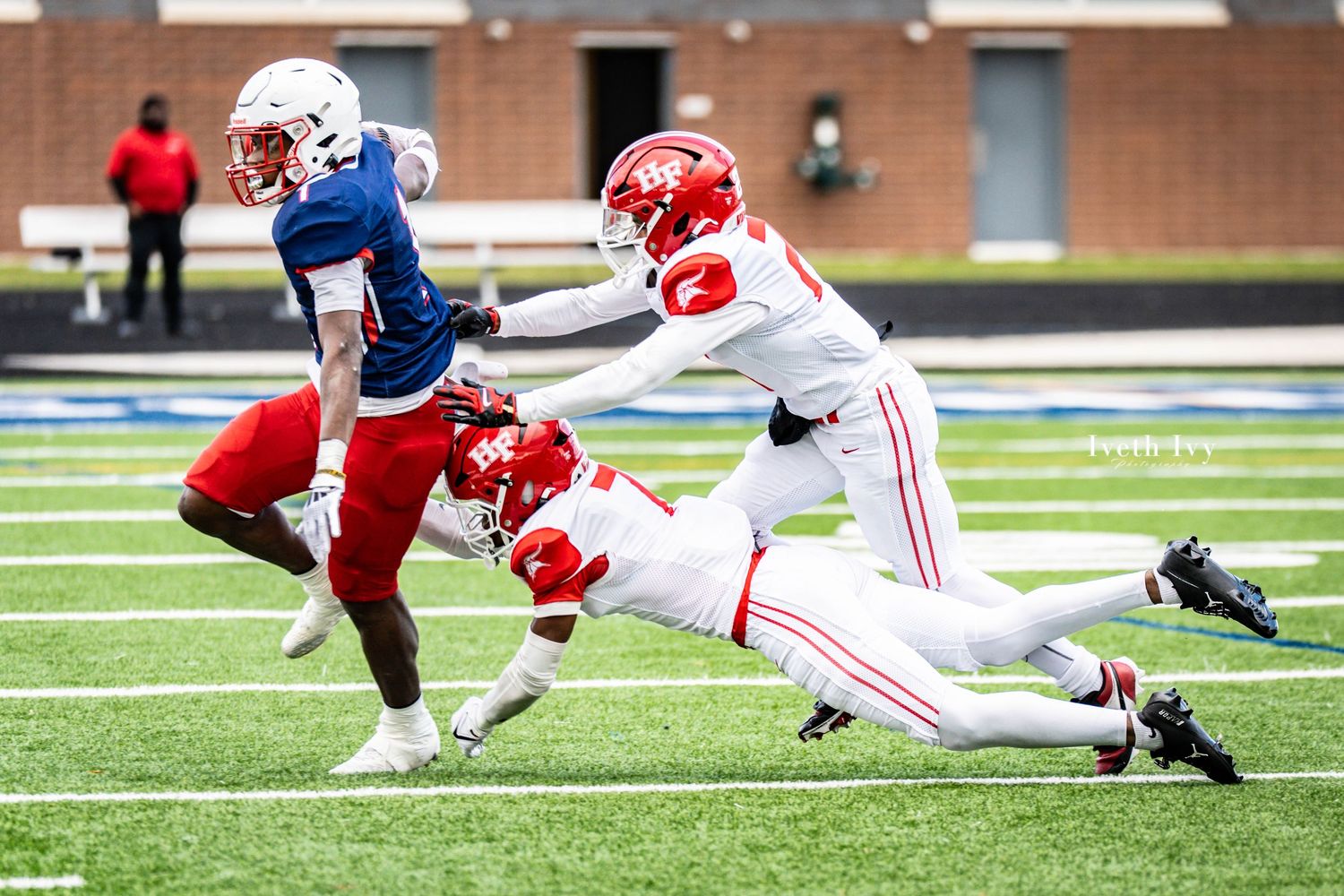 Football players in red and white uniforms dive for a tackle during an intense game play.