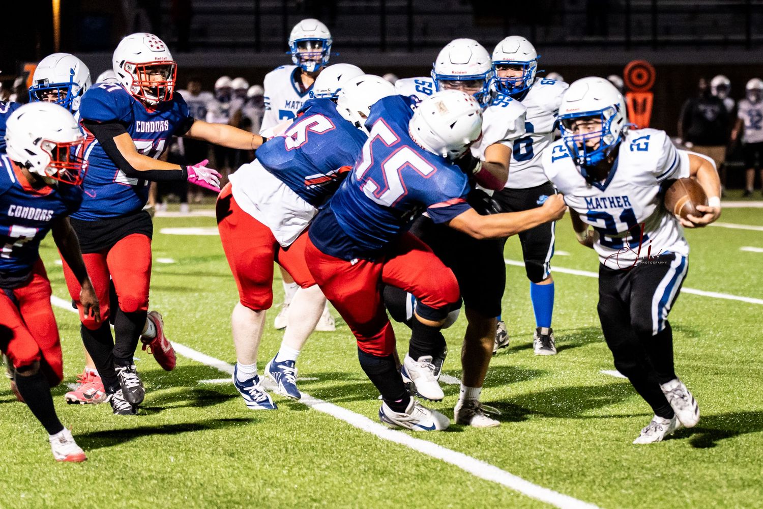 Football players in blue and white uniforms line up in formation during a scrimmage on a sunny field.