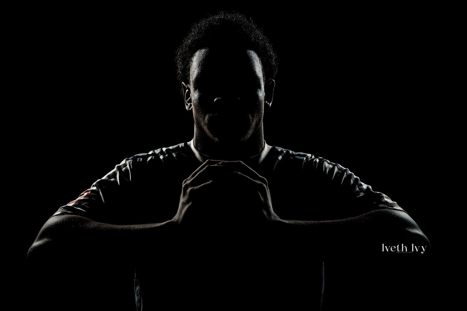 Dramatic silhouette portrait of a male athlete posed with hands together against a dark background.
