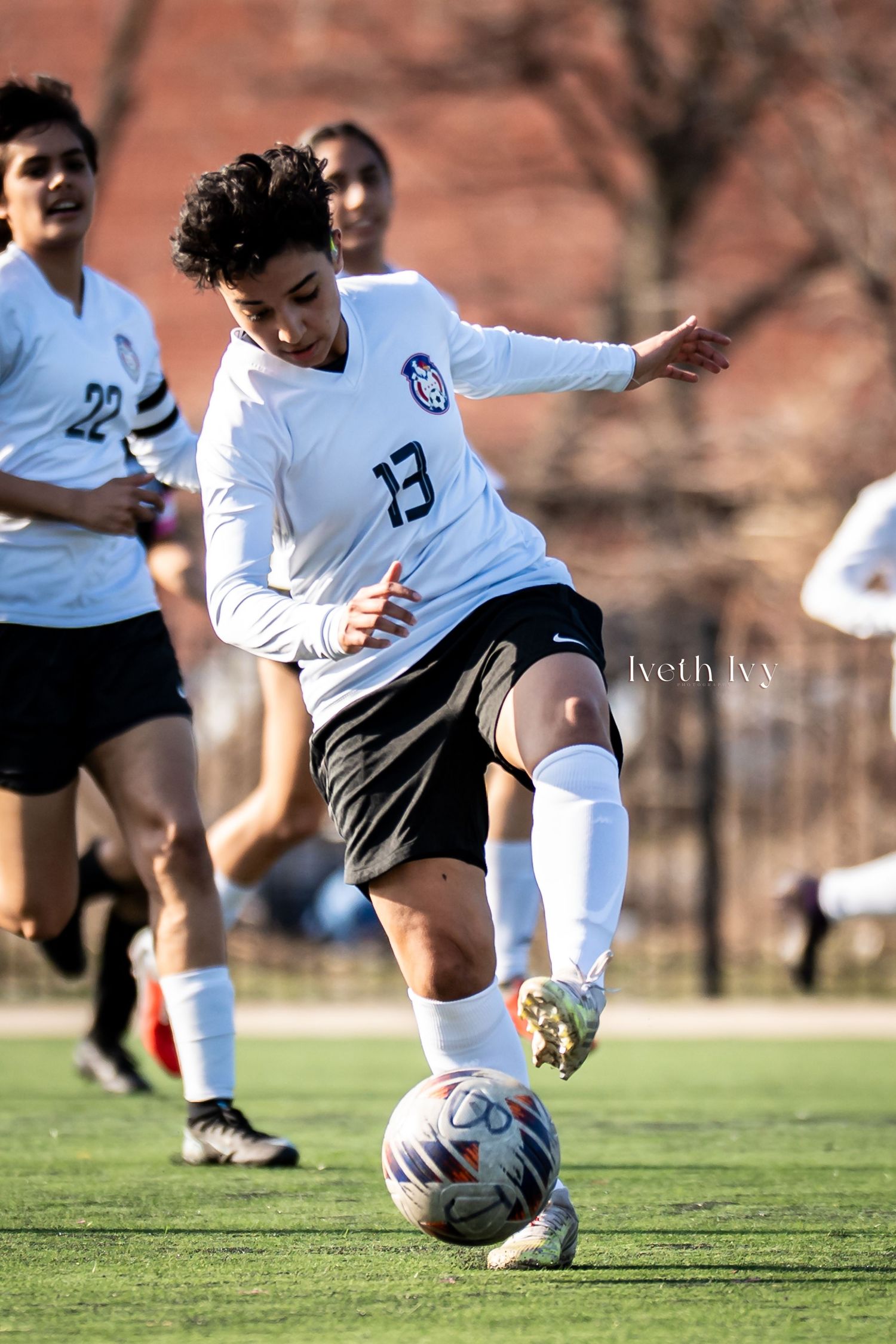 Soccer player wearing jersey number 13 dribbles ball during competitive match on green field.
