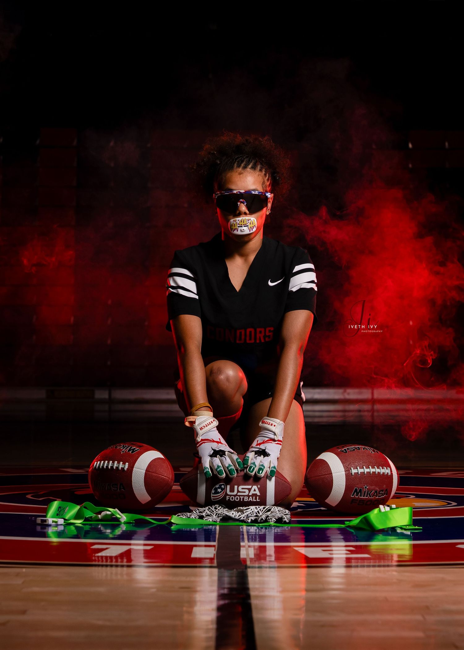 Athlete in black uniform sits on football field with red smoke effect creating dramatic sports photography composition.