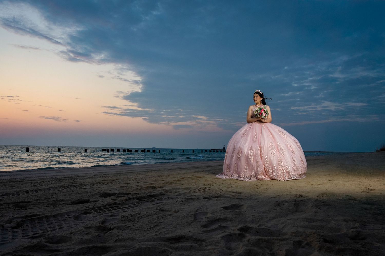 A dreamy sunset photoshoot on the beach with a person wearing a flowing pink ballgown against the dramatic sky.