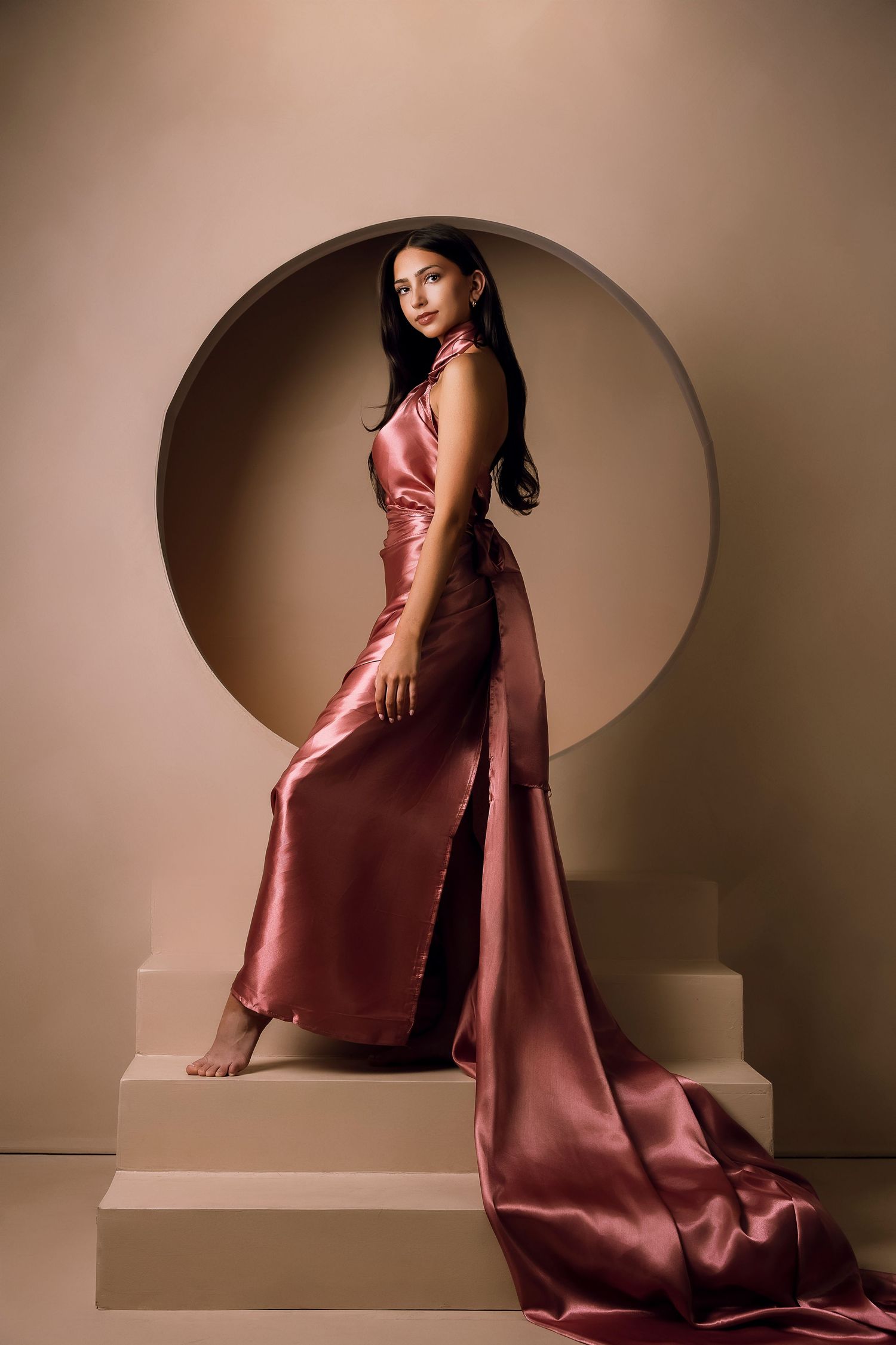 Glamorous satin rose gold evening gown photographed against circular architectural feature.