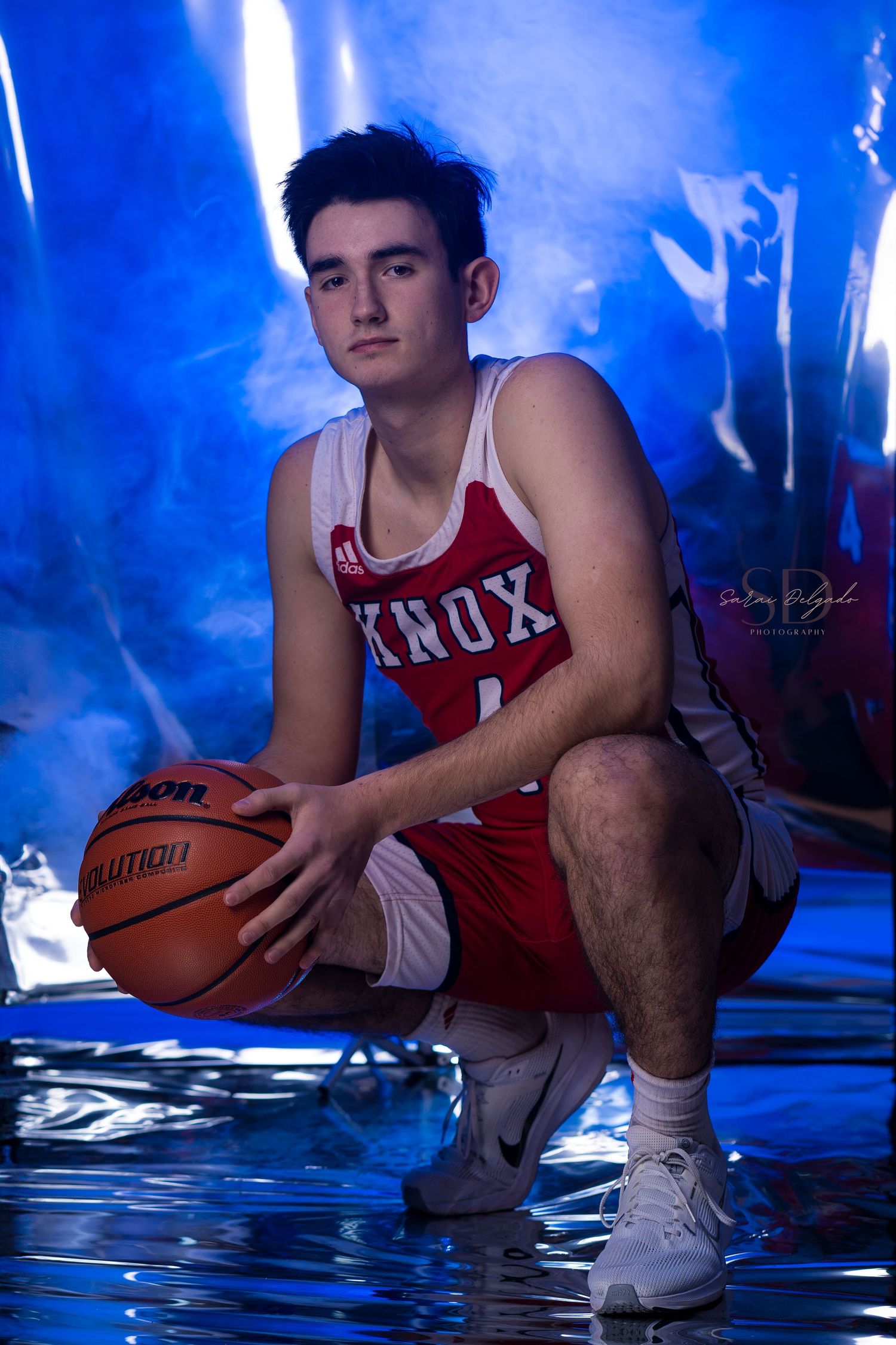 Basketball player in red and white uniform crouches with ball in dramatic blue lighting for sports photography.