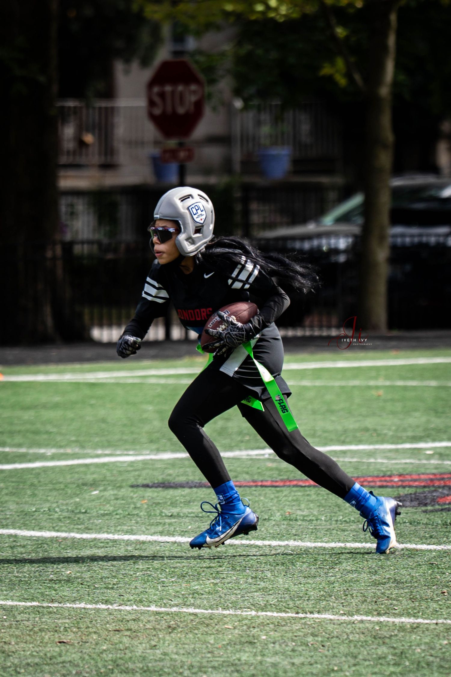 Athlete in black and green uniform performs dynamic running drill on artificial turf field.