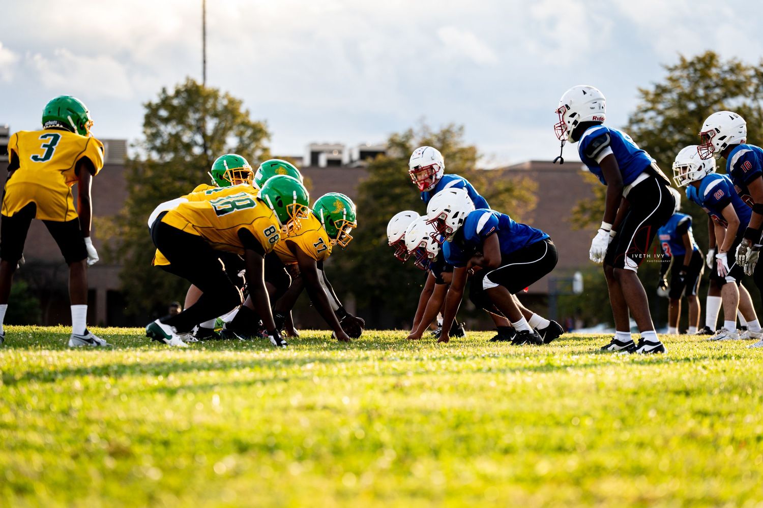Football players line up in formation on a grass field during practice or game preparation.