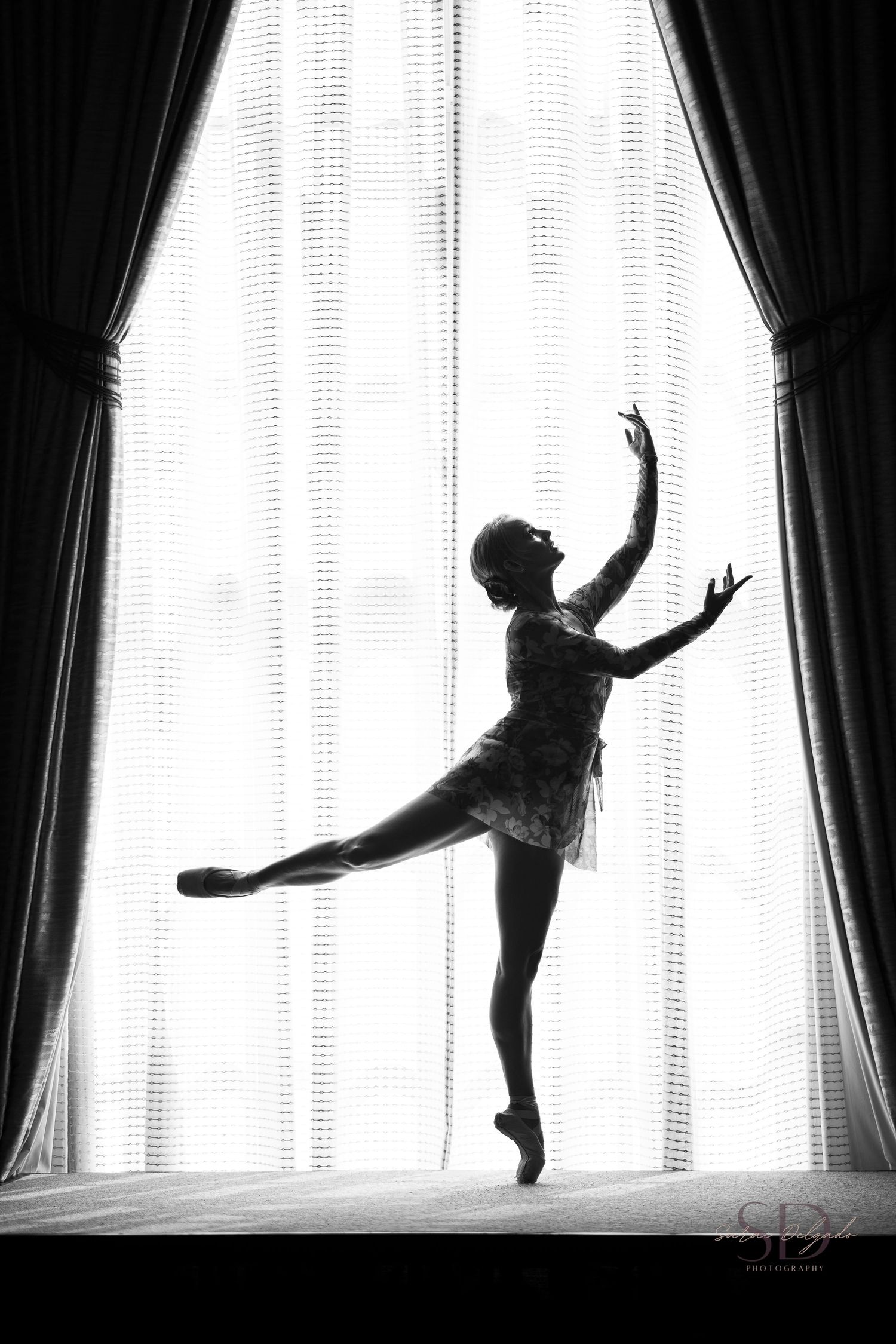 Black and white dance silhouettes against bright window with curtains.