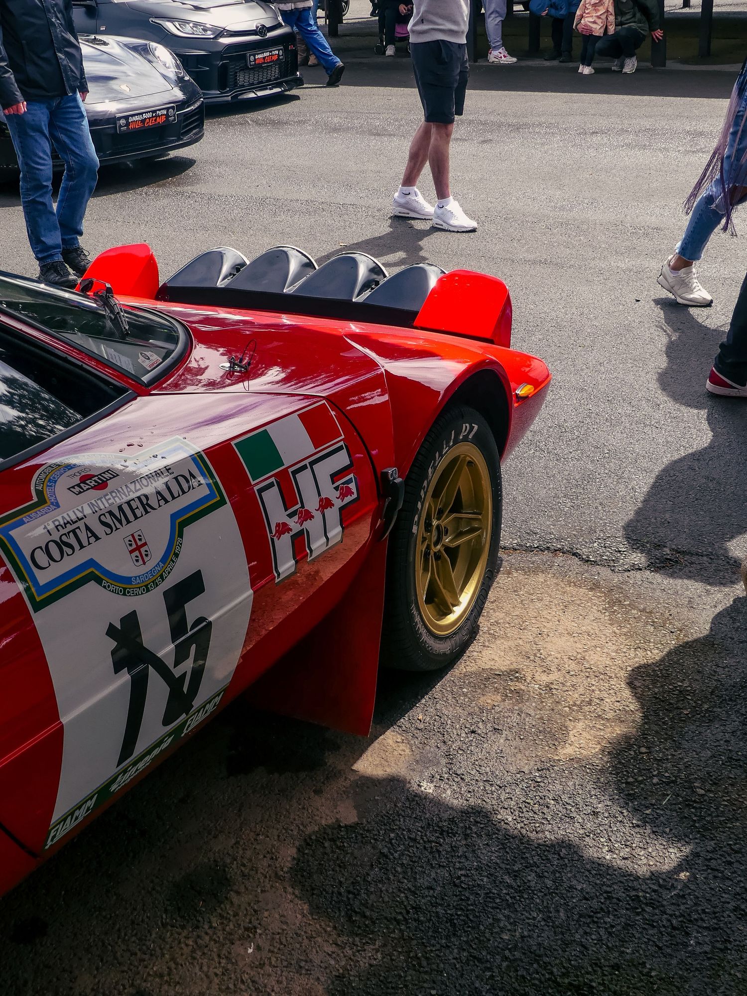 Red vintage racing car with gold wheels and racing numbers displayed at a car show.