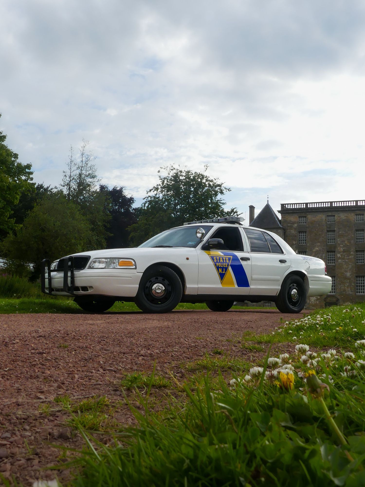 State police vehicle positioned on a dirt road with wildflowers and a stone castle in the background.