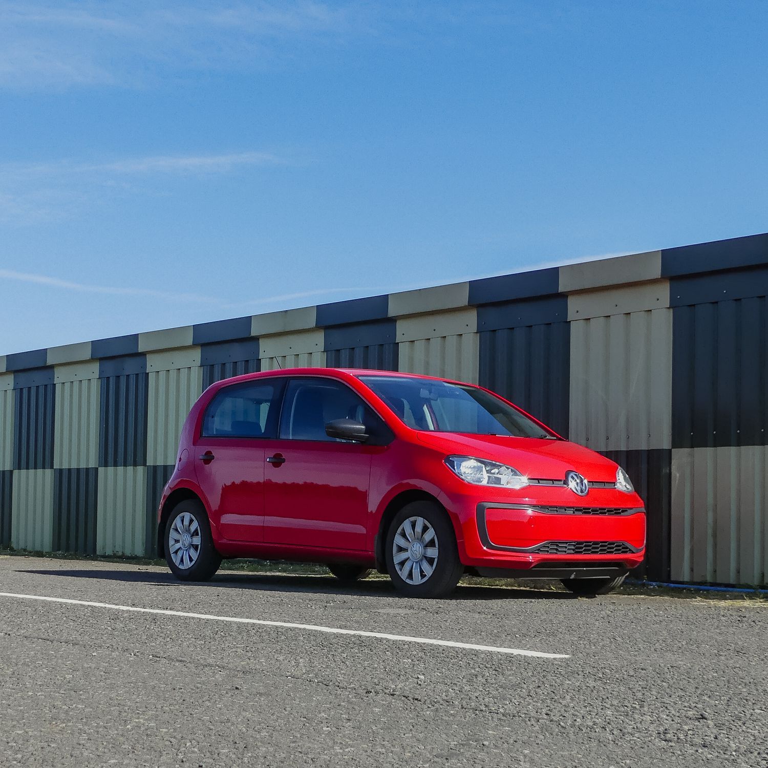 Red Volkswagen Golf lineup photographed in a parking lot against industrial storage units on a sunny day.