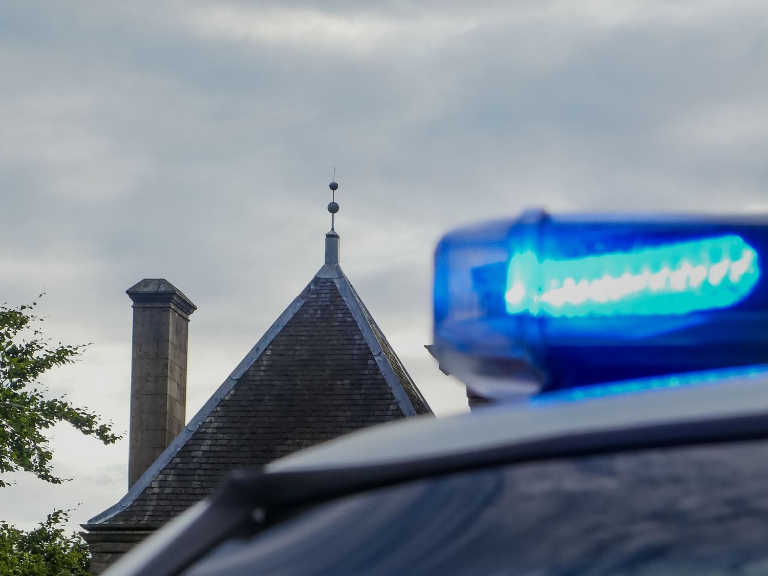 Blue emergency lights on top of a police vehicle against an overcast sky.