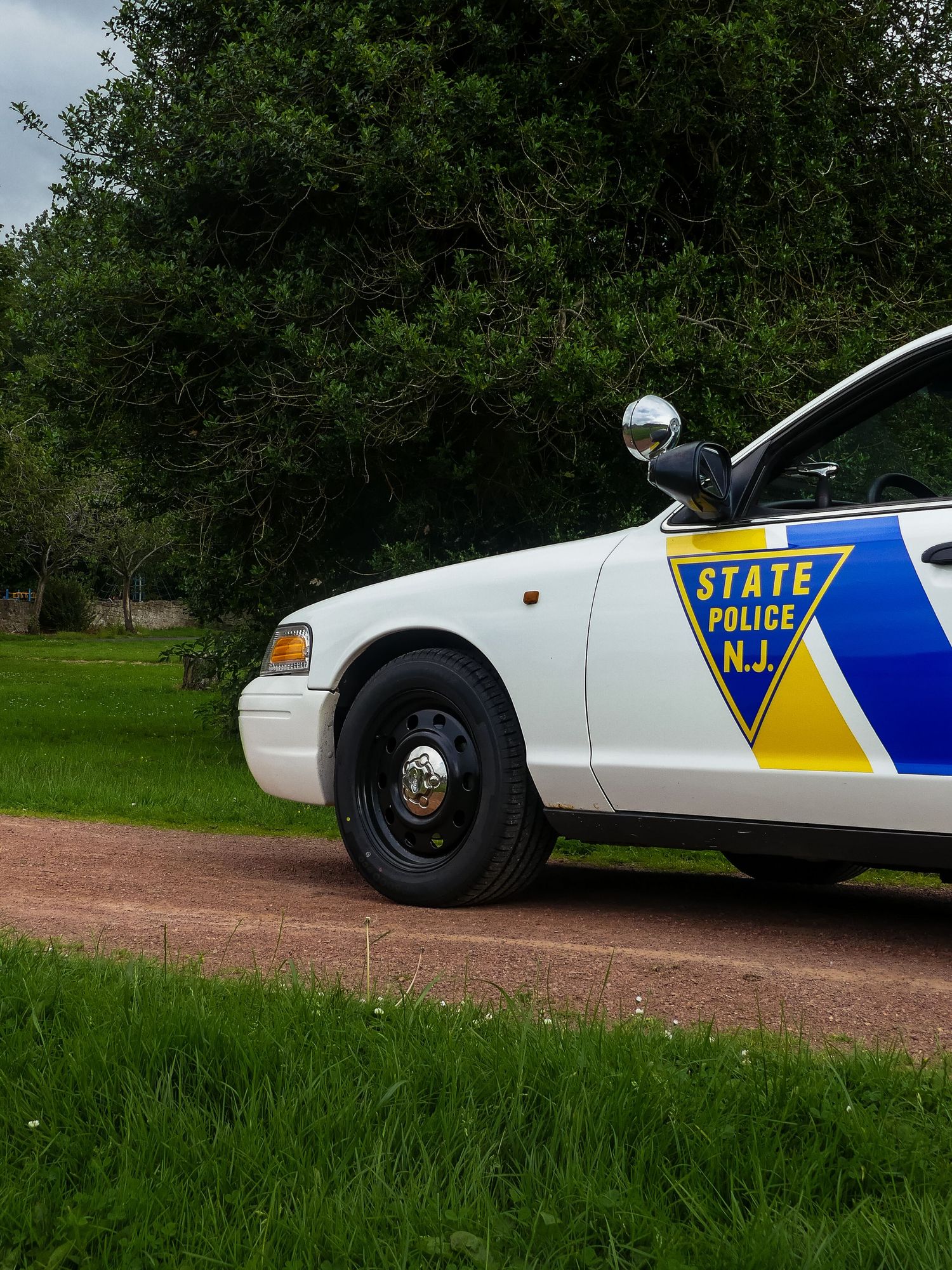 Close-up side views of a New Jersey State Police patrol car parked on a dirt road with grassy surroundings.