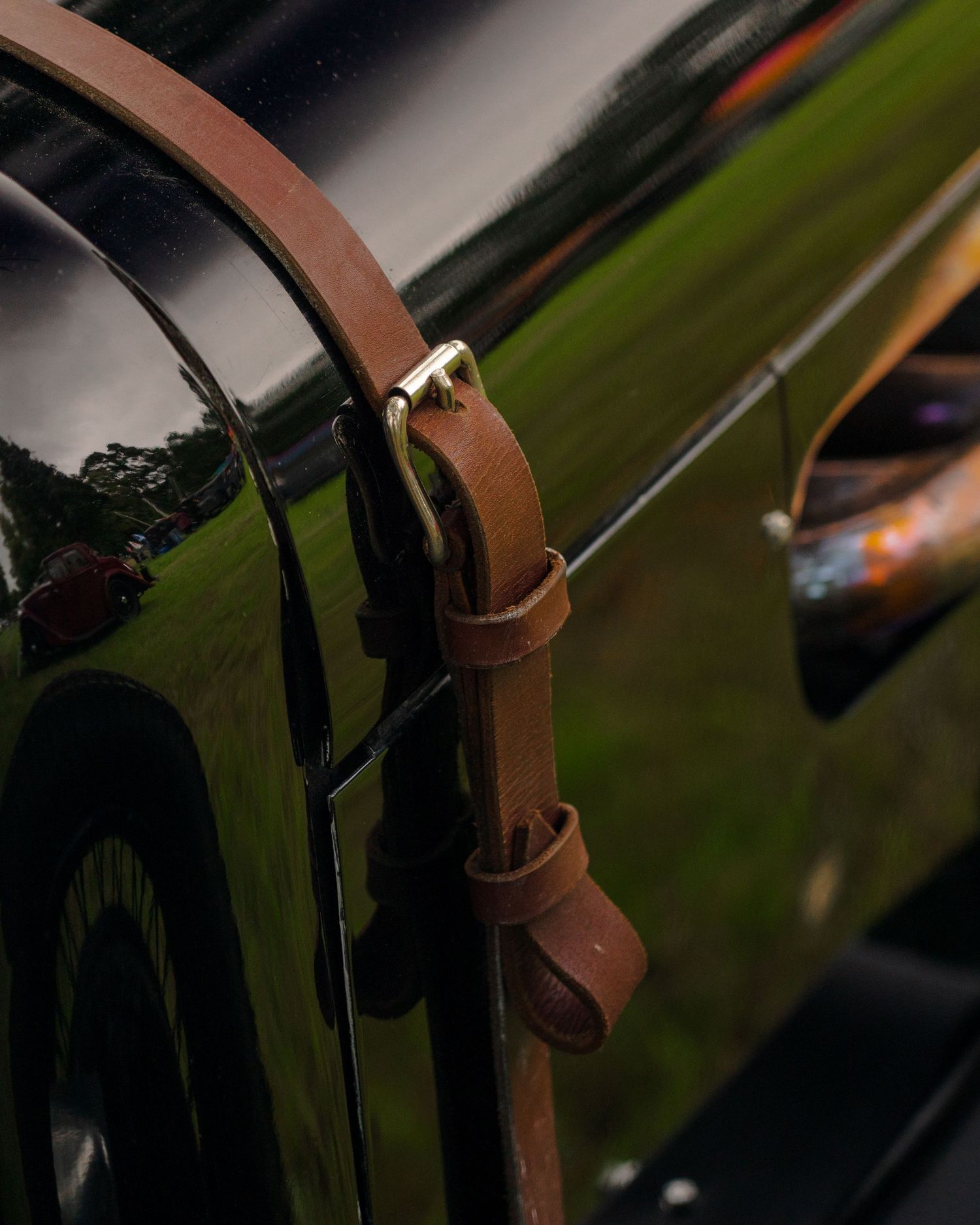 Close-up of a tan leather buckle strap on a glossy dark green vintage car exterior.