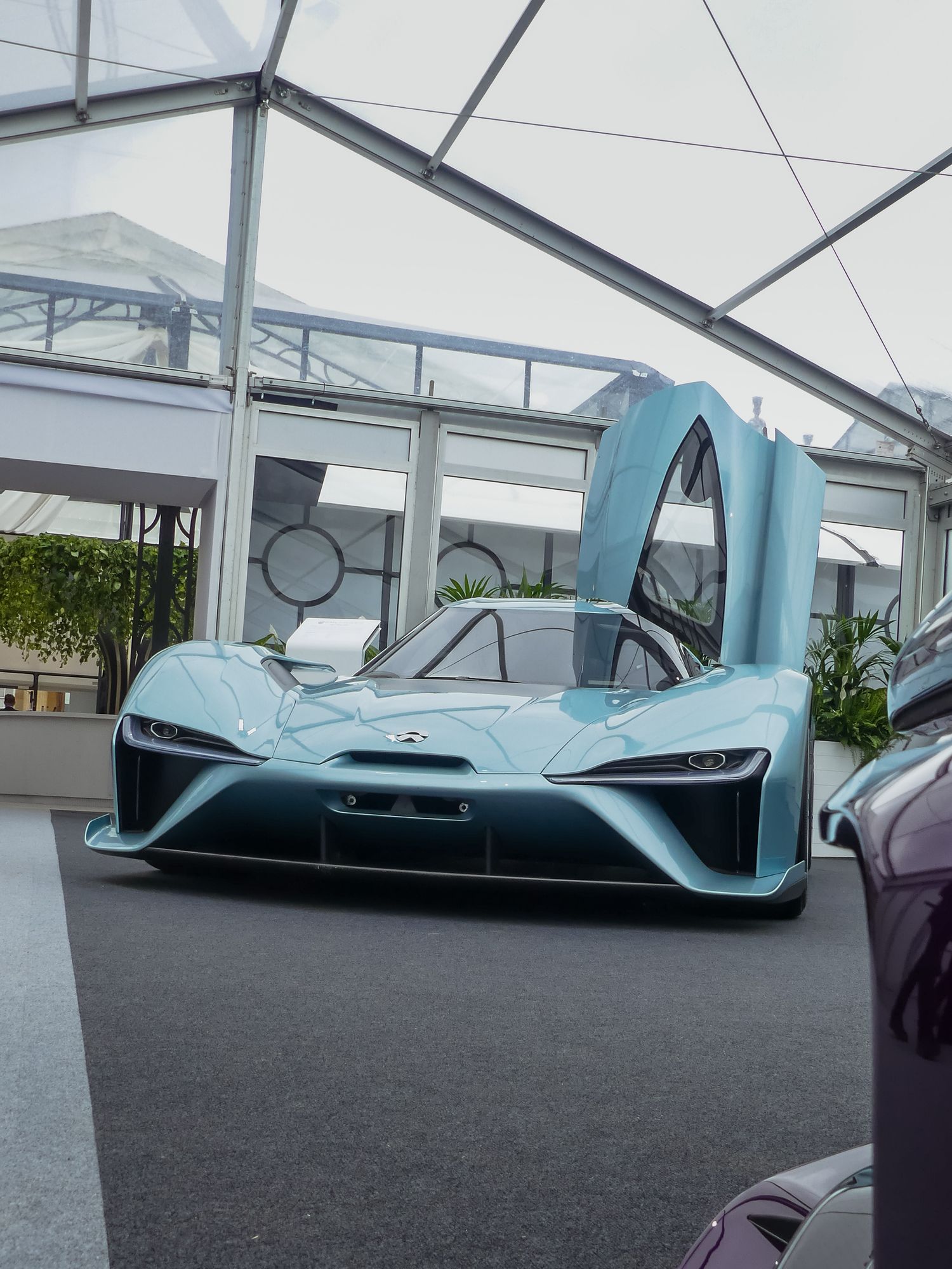 Light blue NIO EP9 electric supercar with dramatic butterfly doors displayed in a modern showroom setting.