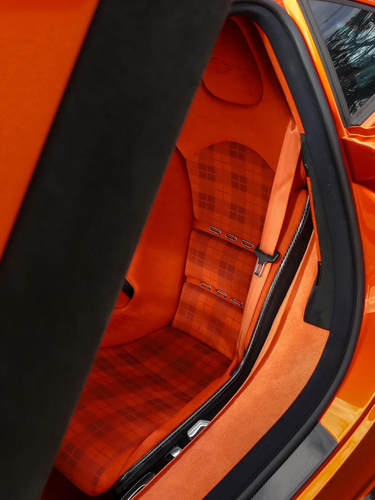 Interior view of a luxury car seat with orange leather upholstery and plaid fabric pattern details.