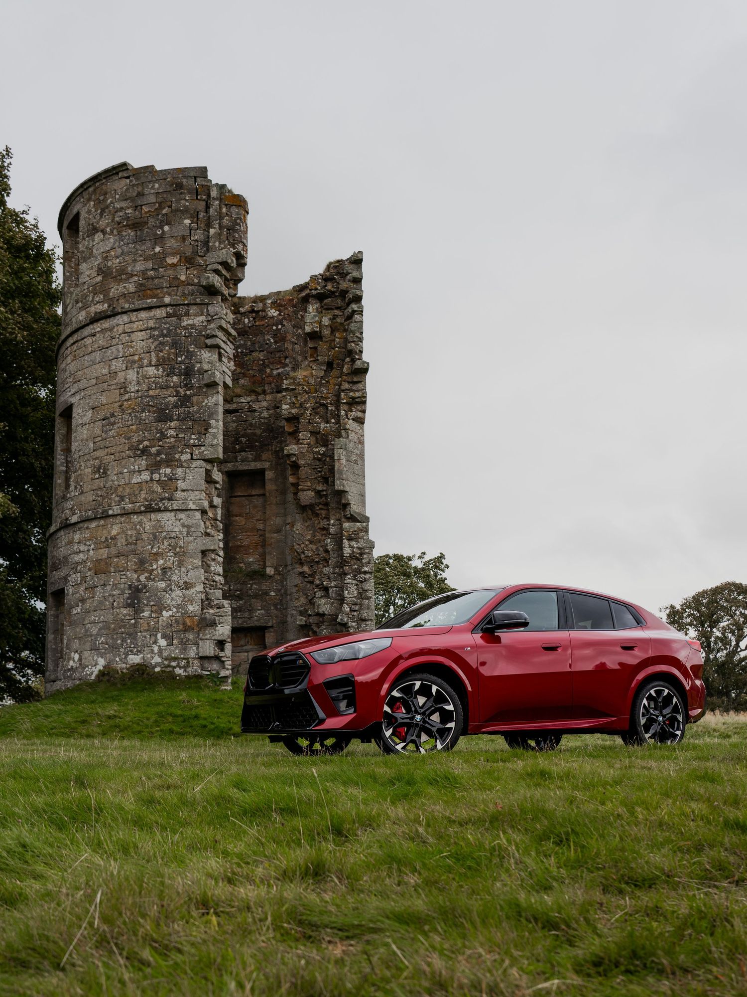 A red Toyota RAV4 SUV parked beside ancient stone castle ruins on a grassy hillside.
