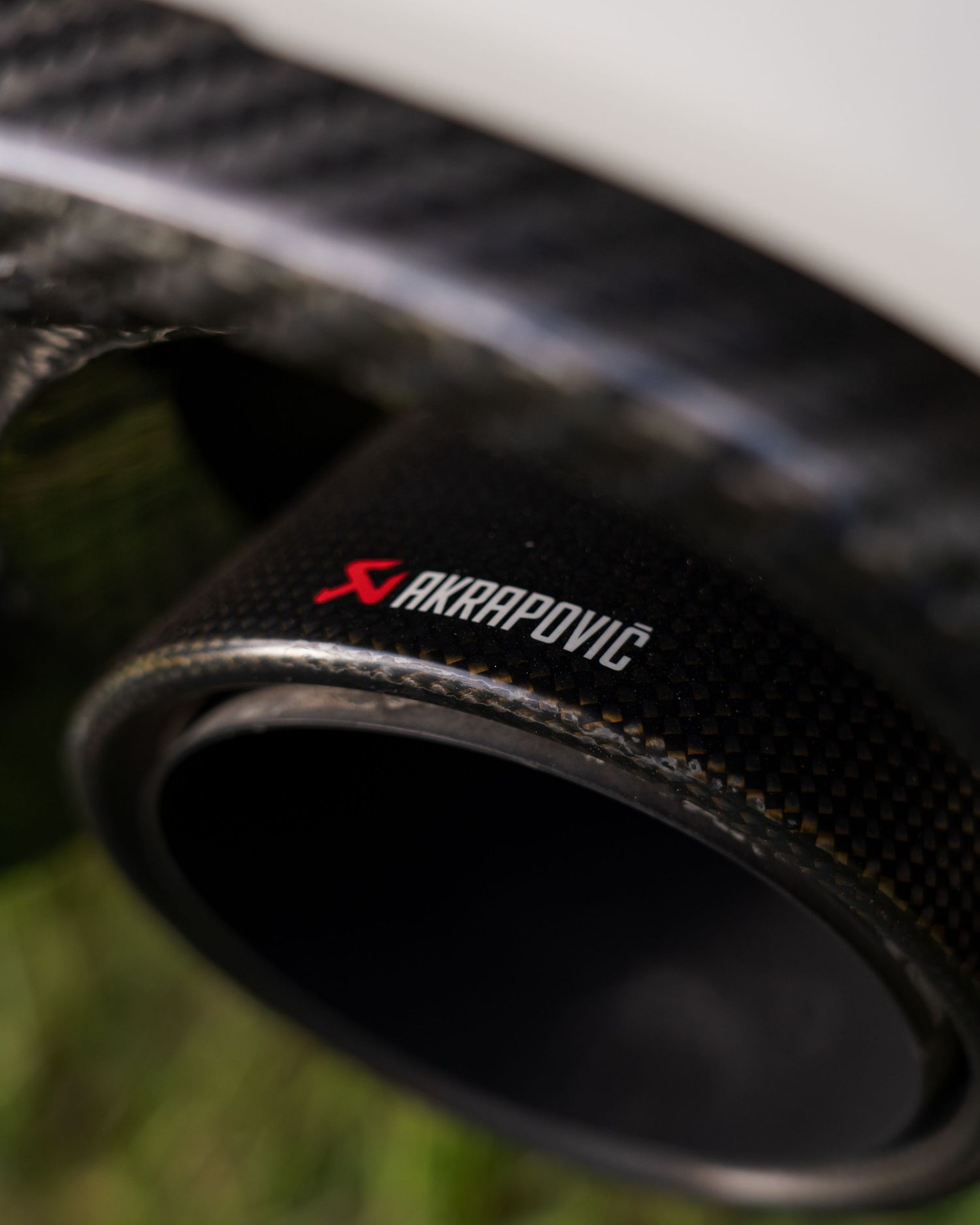 Close-up of an Akrapovic carbon fiber exhaust tip on a performance vehicle exhaust system.