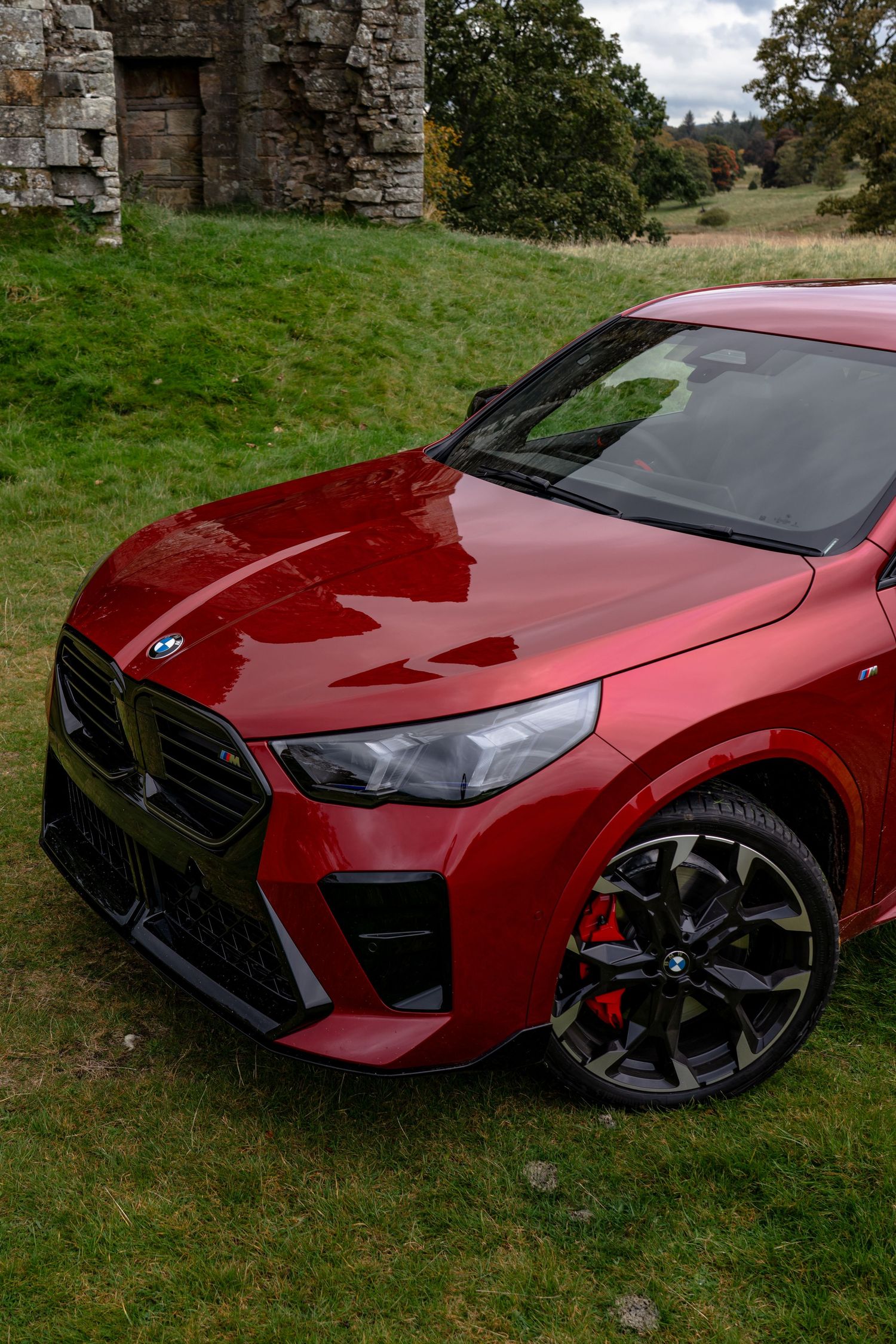 A red Kia Stinger GT sports car photographed from multiple angles on grass near a stone wall.