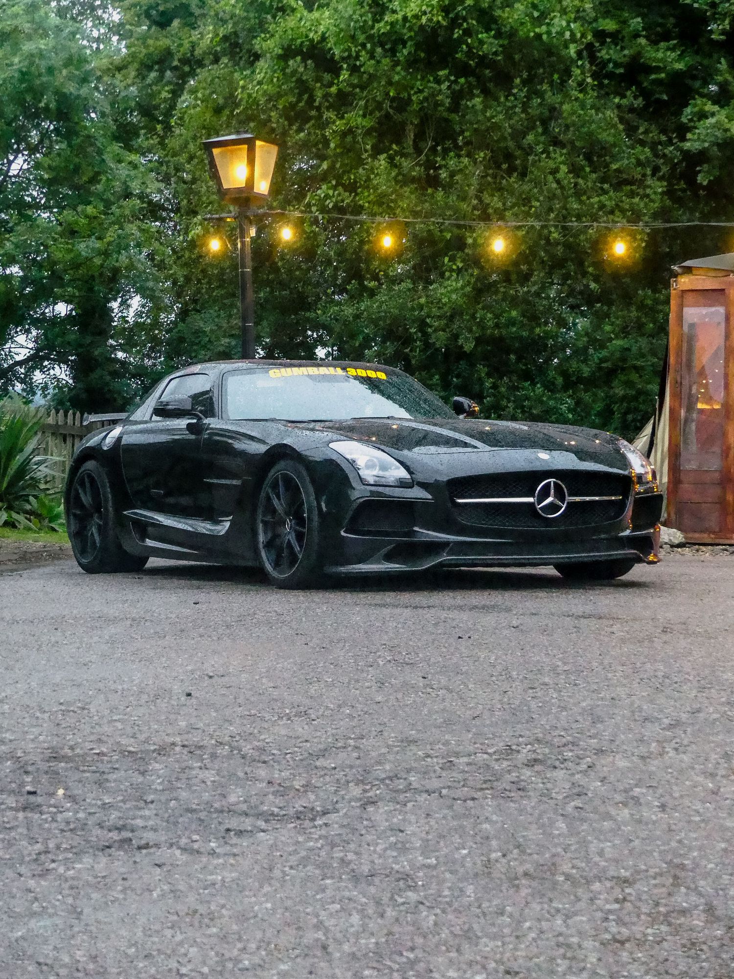 A sleek black Mercedes concept car parked on gravel path with glowing lanterns illuminating the scene at dusk.