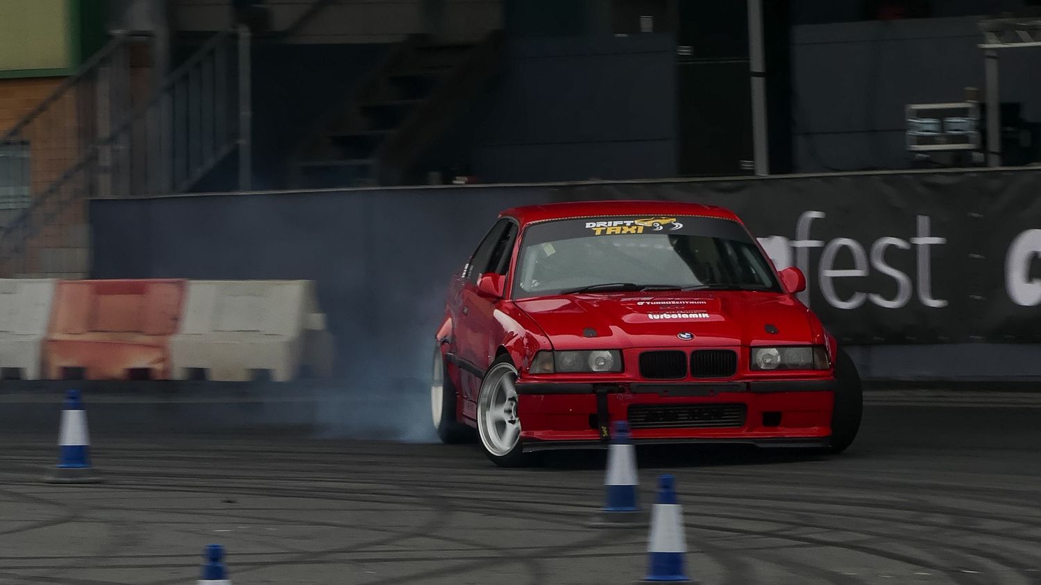 Red BMW drifting through blue cones during a motorsport event.