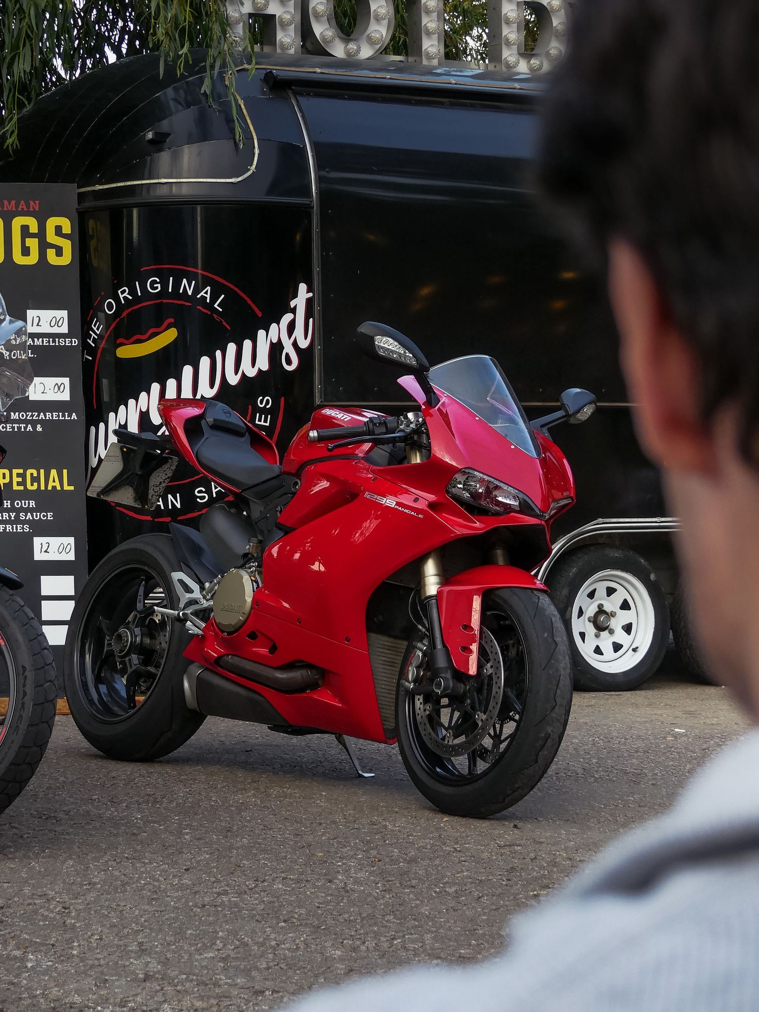 A bright red Ducati Panigale motorcycle parked in front of a food truck with signage.
