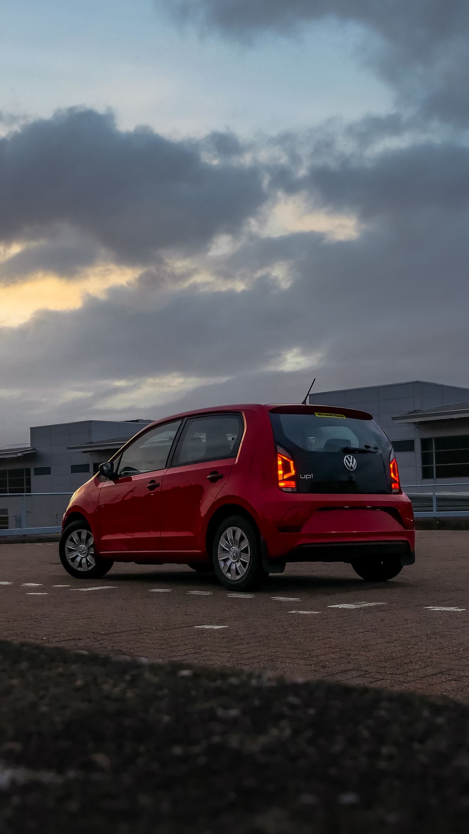 Red Volkswagen UP parked at sunset with dramatic cloudy sky in the background.