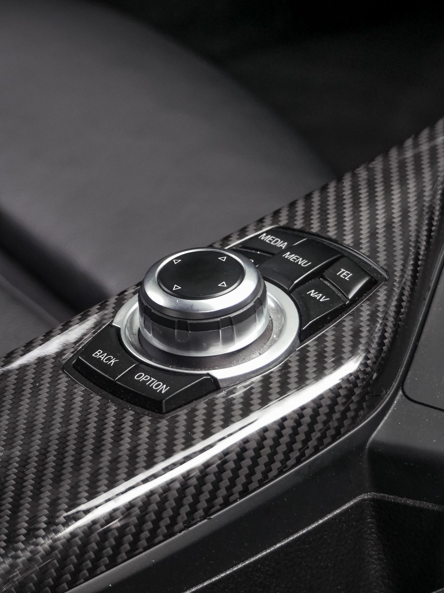 Close-up view of a modern car's iDrive controller with carbon fiber trim and metallic finish controls.