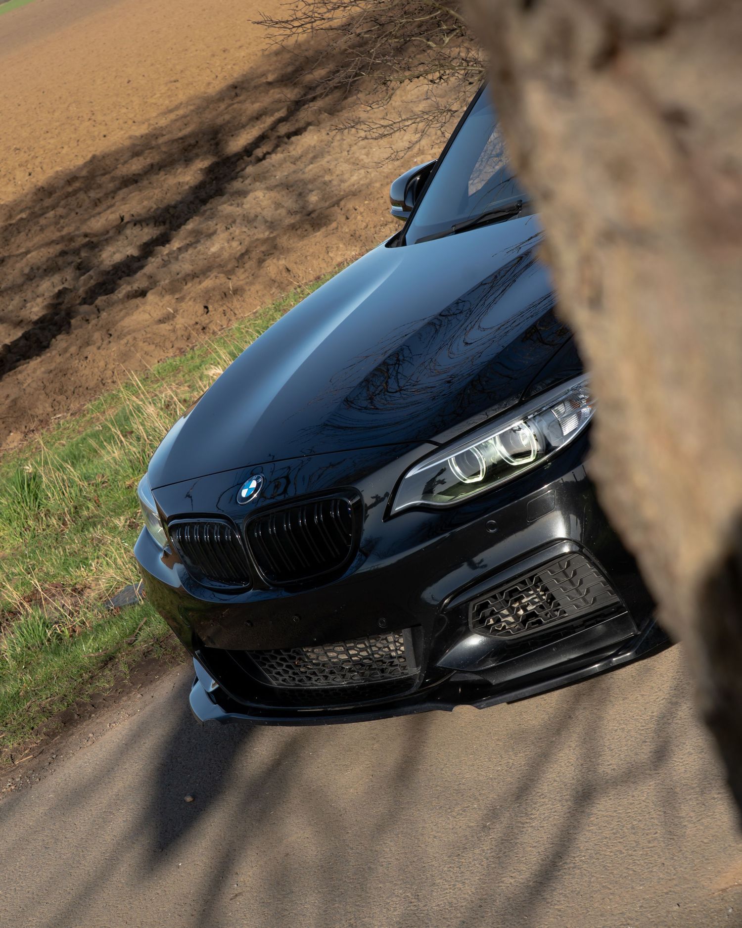 Black BMW 2 Series coupe photographed from above on a rural road, showcasing its sleek front grille and hood design.