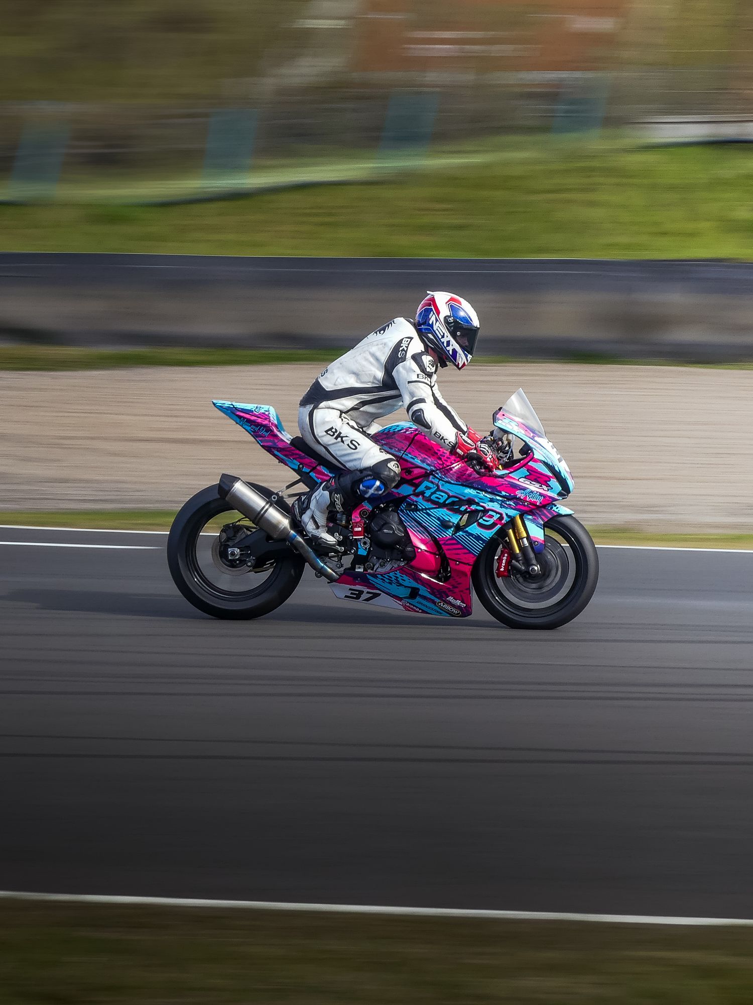 A motorcycle rider racing on a colorful sport bike with pink and blue graphics speeds around a racetrack during competition.
