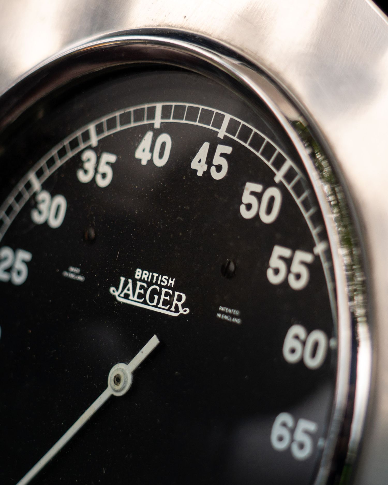 Close-up of a vintage British Jaeger black-faced speedometer with chrome bezel showing numbers 25 to 65.