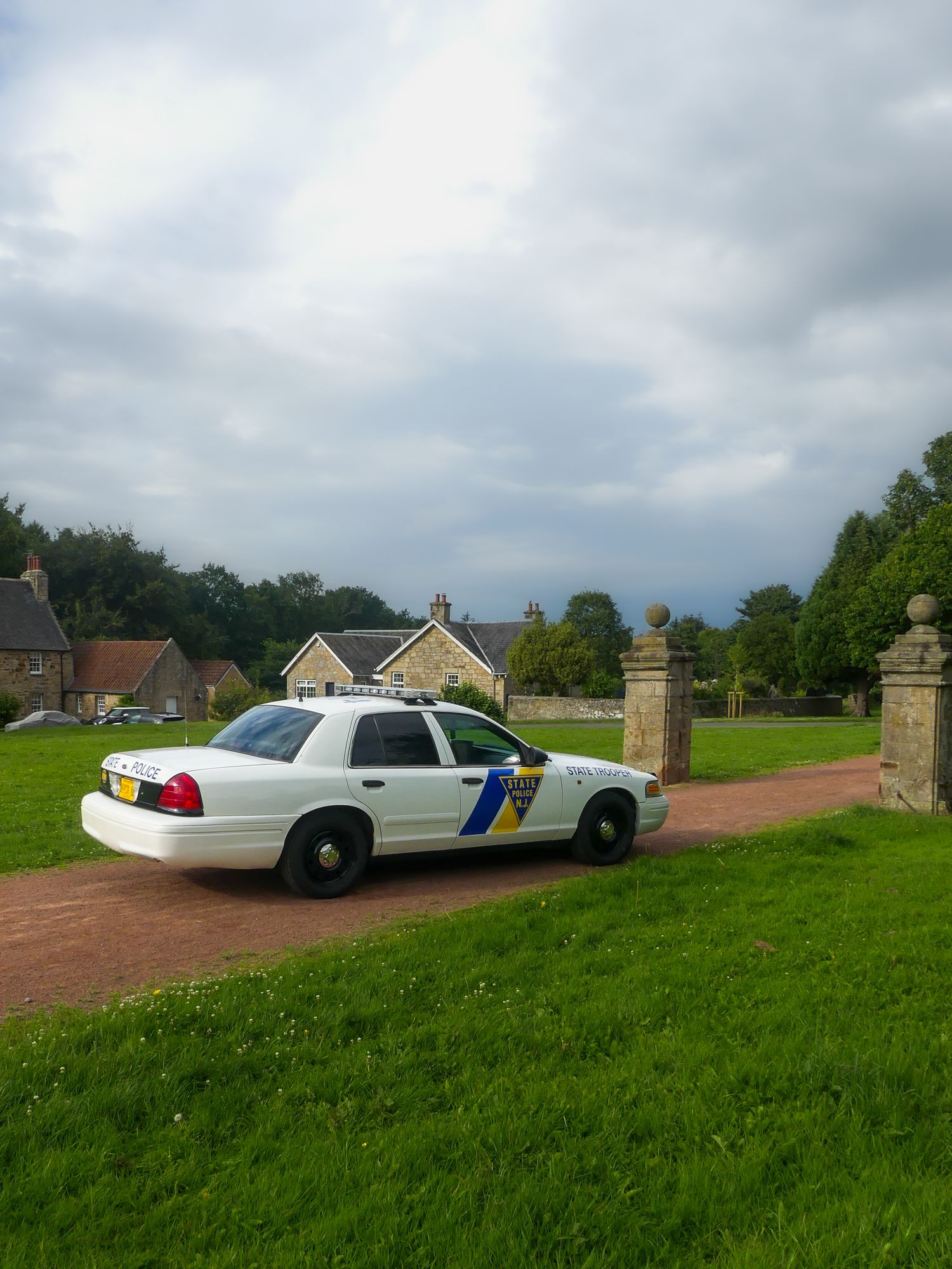 A pair of white police patrol cars parked on a grassy area near stone pillars and residential buildings.