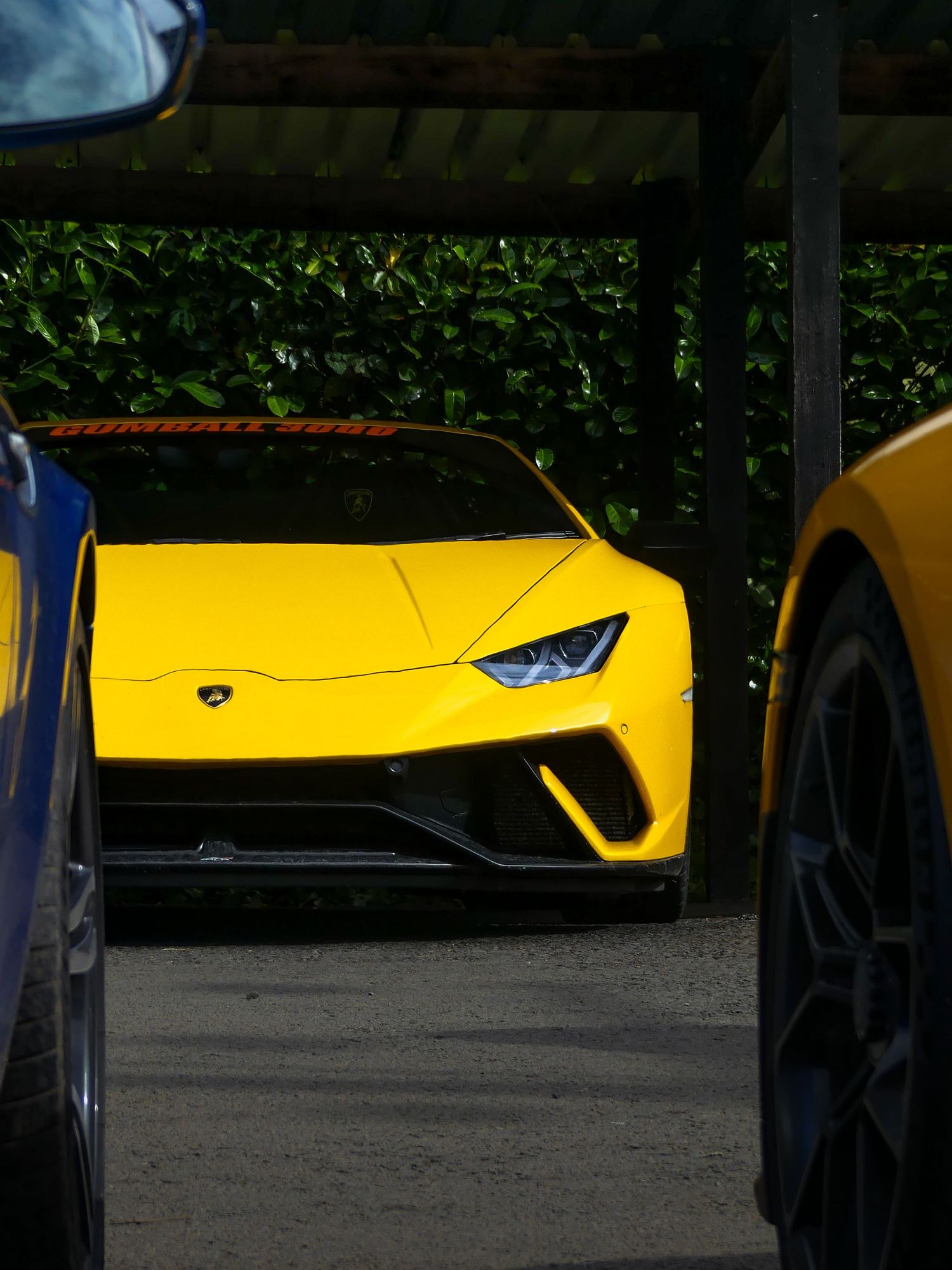 A bright yellow Lamborghini Huracan sports car partially visible under a covered parking area.