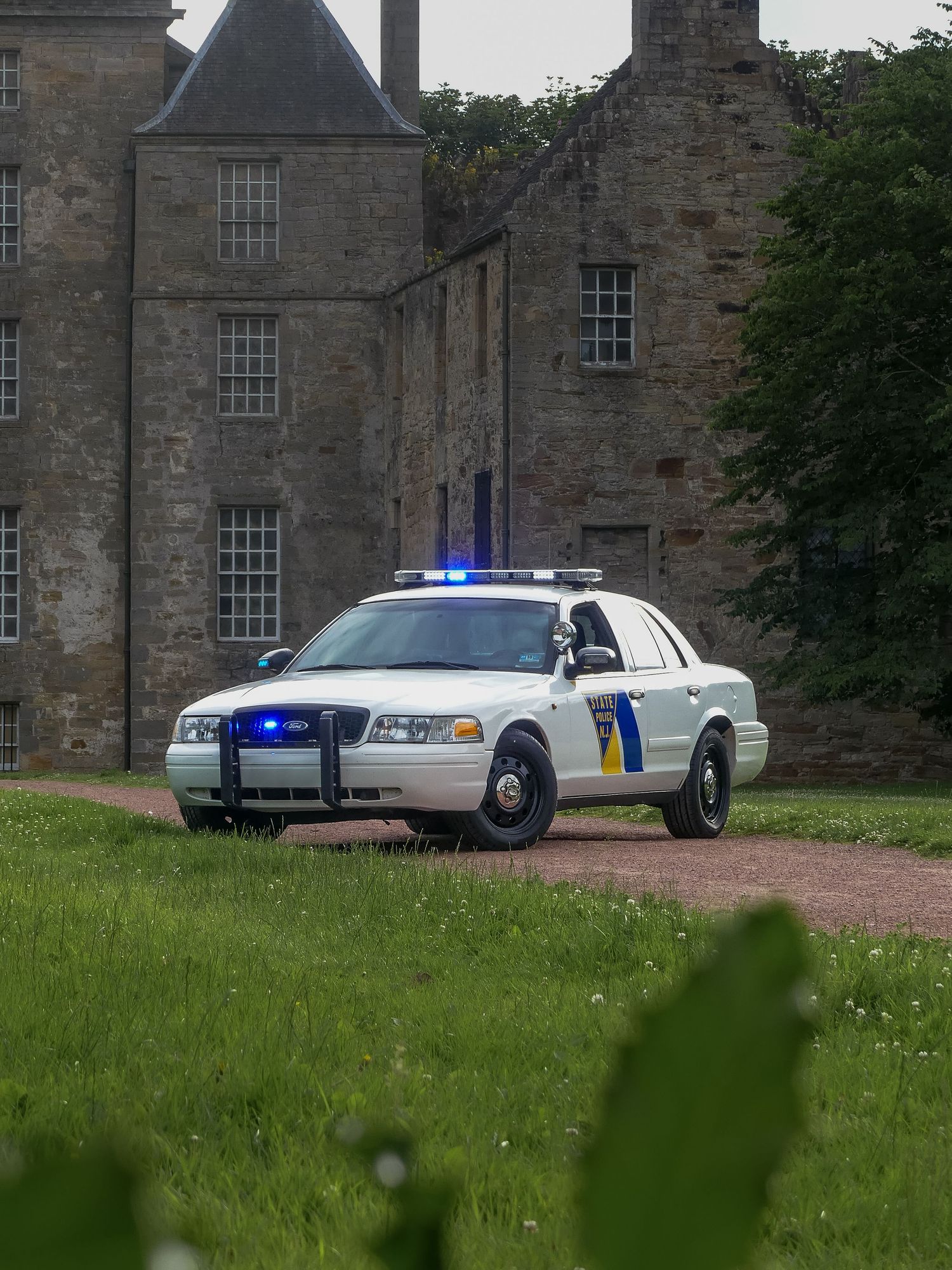 A white State Trooper police car parked in front of a historic stone castle-like building with blue emergency lights on.