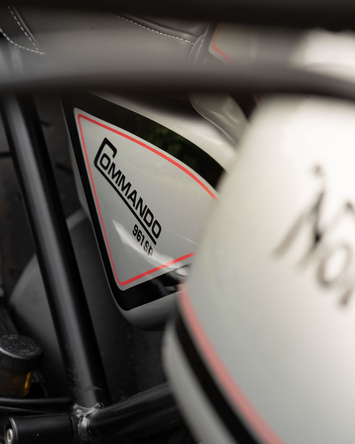 Close-up of a Norton Commando 961 SP motorcycle tank badge with red and black detailing on a white fairing.