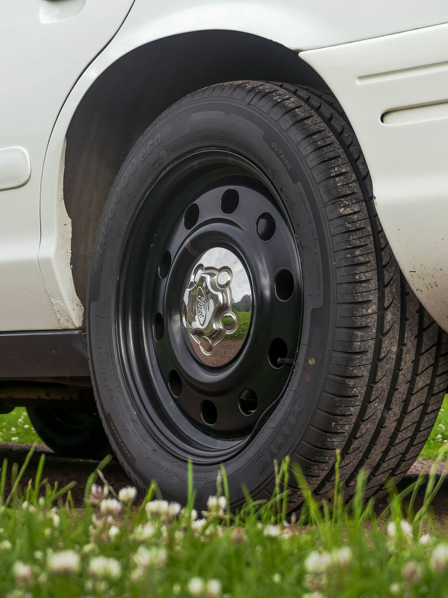 Close-up of a black steel wheel and tire on a police vehicle surrounded by grass and daisies.