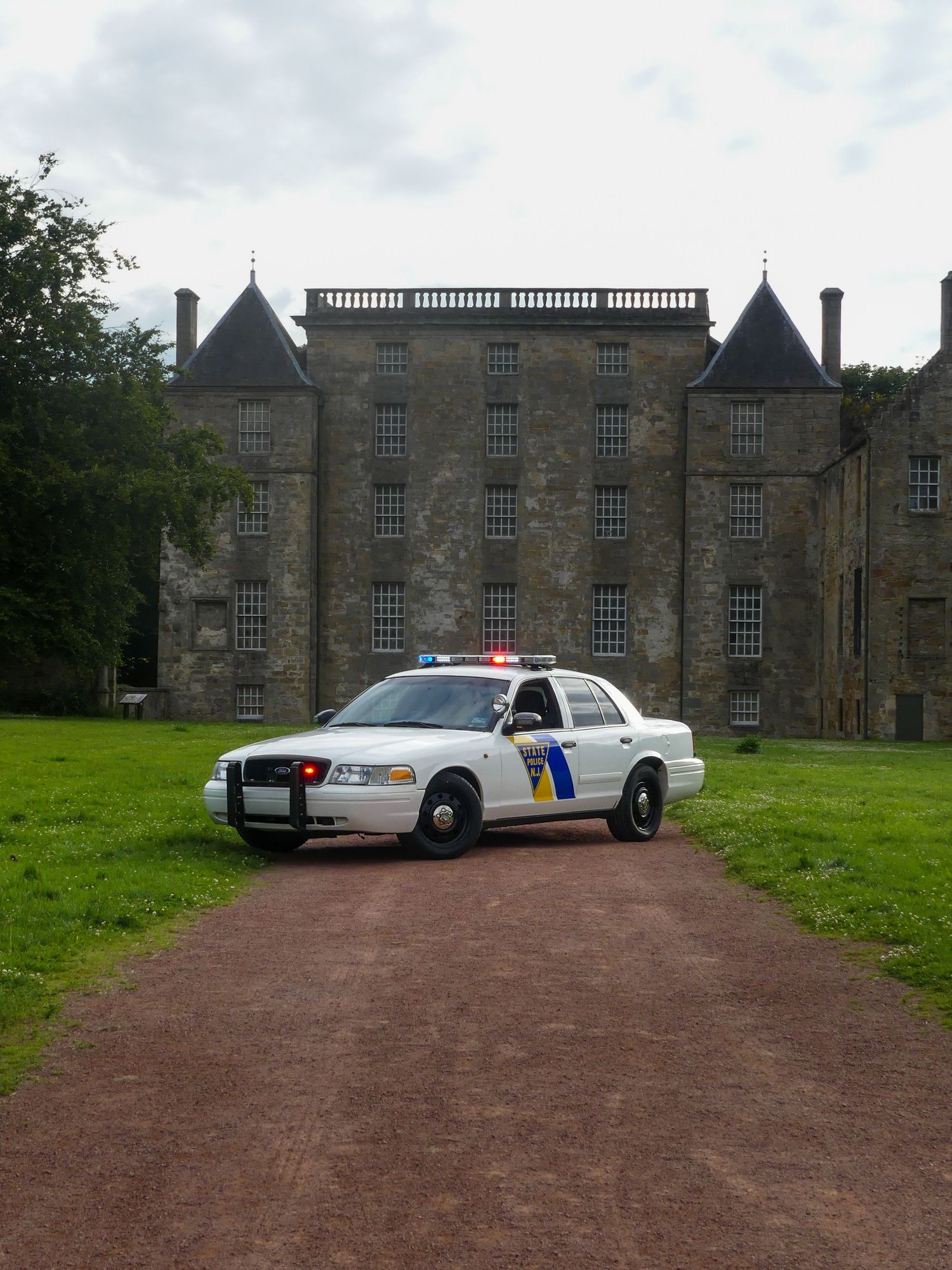 A white Ford Crown Victoria police car positioned on a dirt path before an imposing Scottish castle.