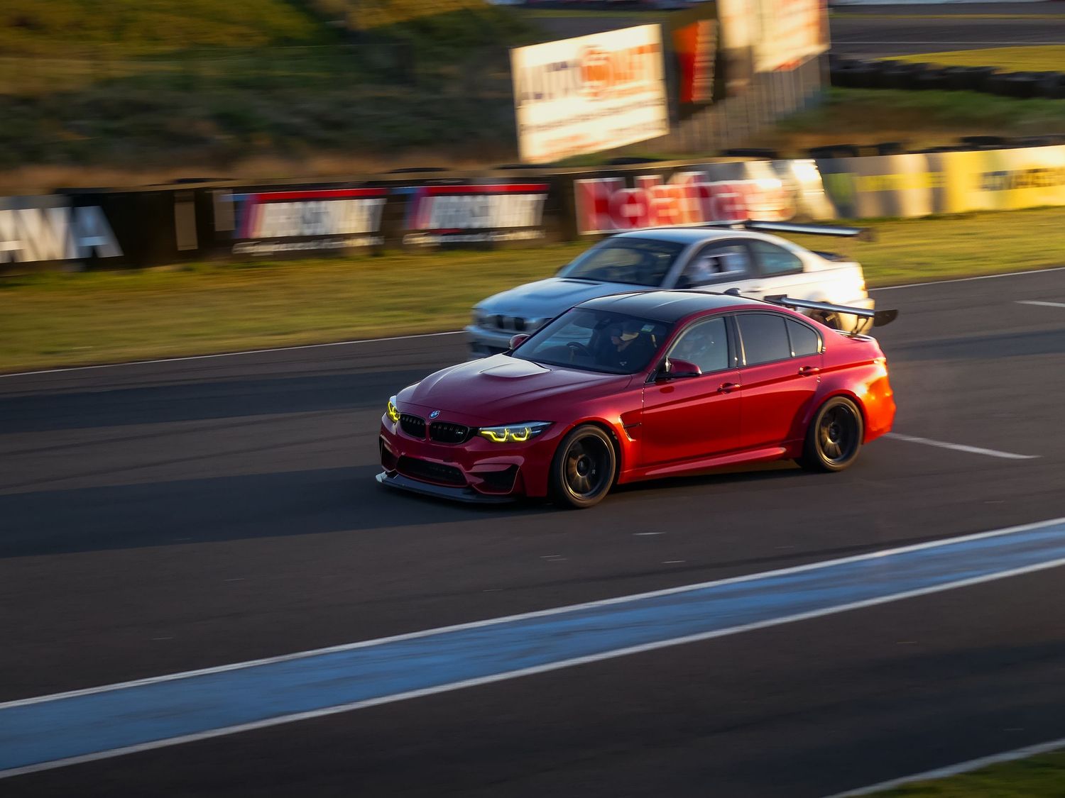 Performance cars race along a winding mountain road at sunset as part of a spirited driving session.