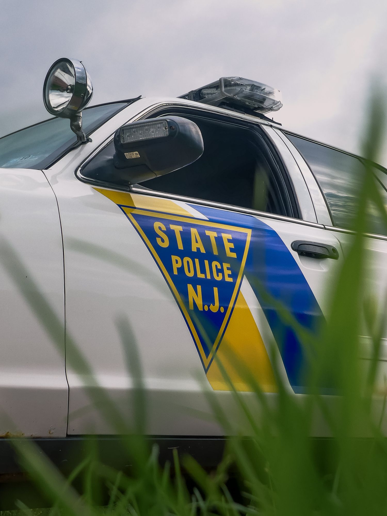 Close-up view of New Jersey State Police car markings showing blue and yellow striped decals on white vehicle body.