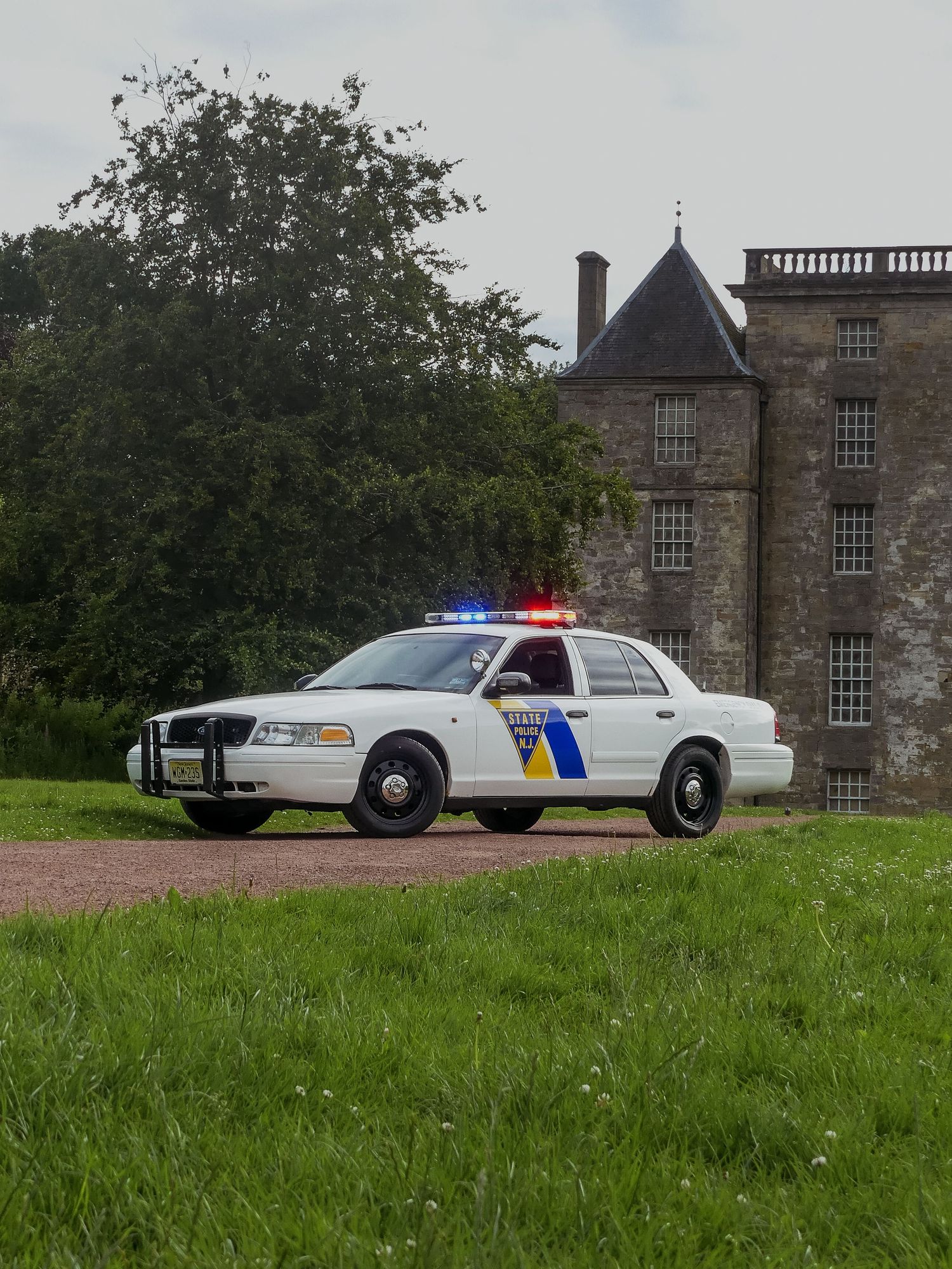 A vintage police patrol car parked on grass in front of a historic stone castle or mansion building.