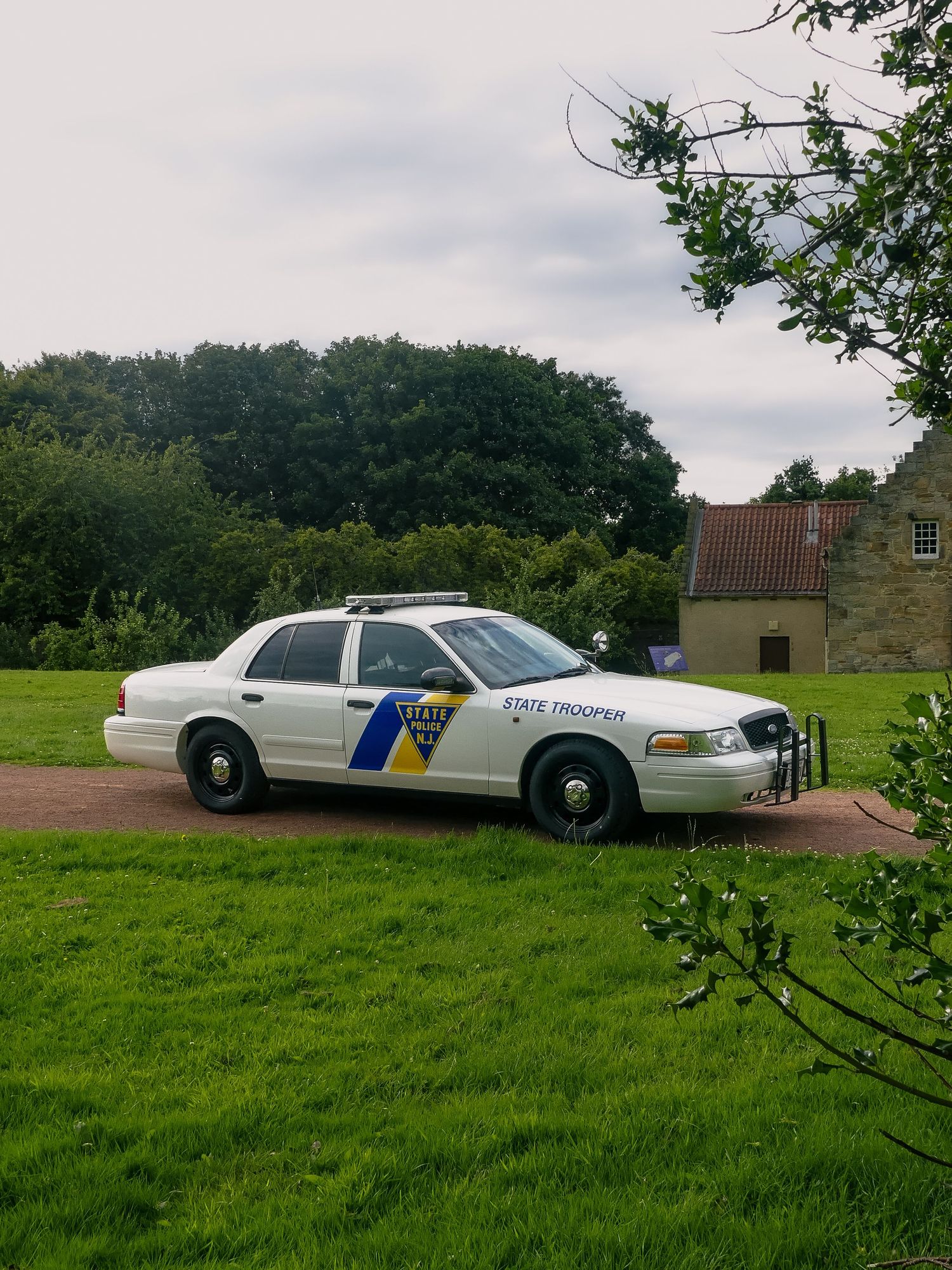 White New Jersey State Police patrol car parked on grass near a stone building.