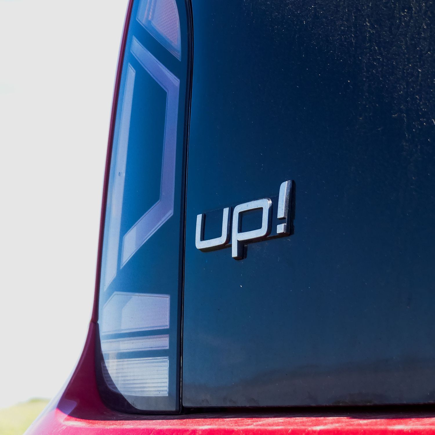 Close-up detail of a modern Volkswagen up! badge on dark blue car exterior panel.