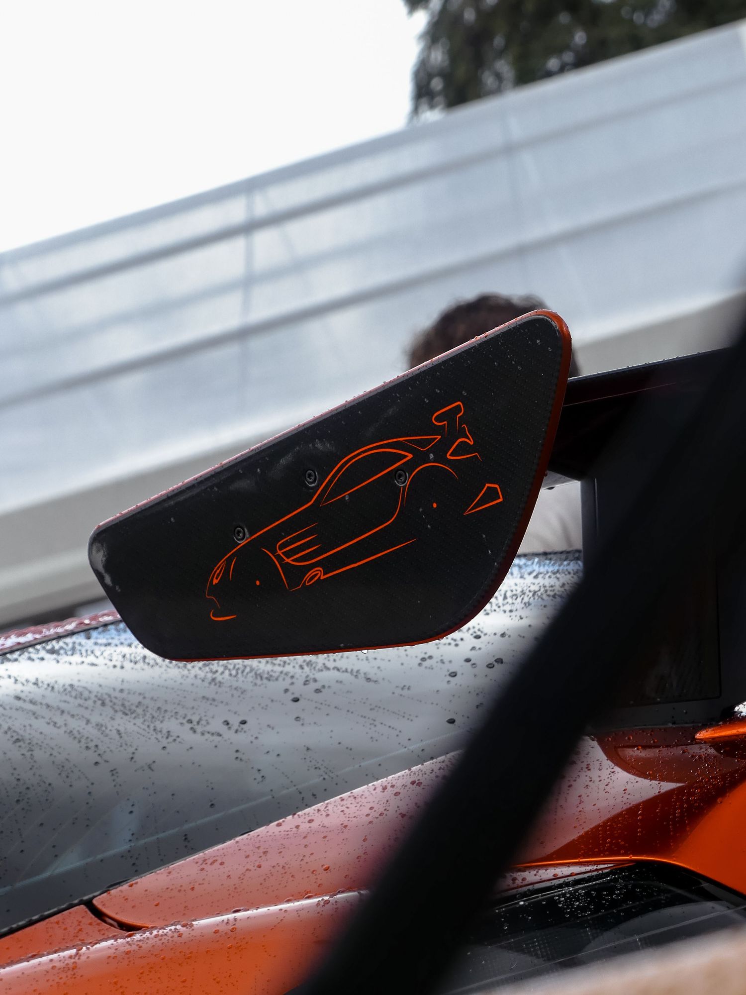 Red McLaren F1 sports car silhouette logo design appears on dark surface with water droplets for dramatic effect.