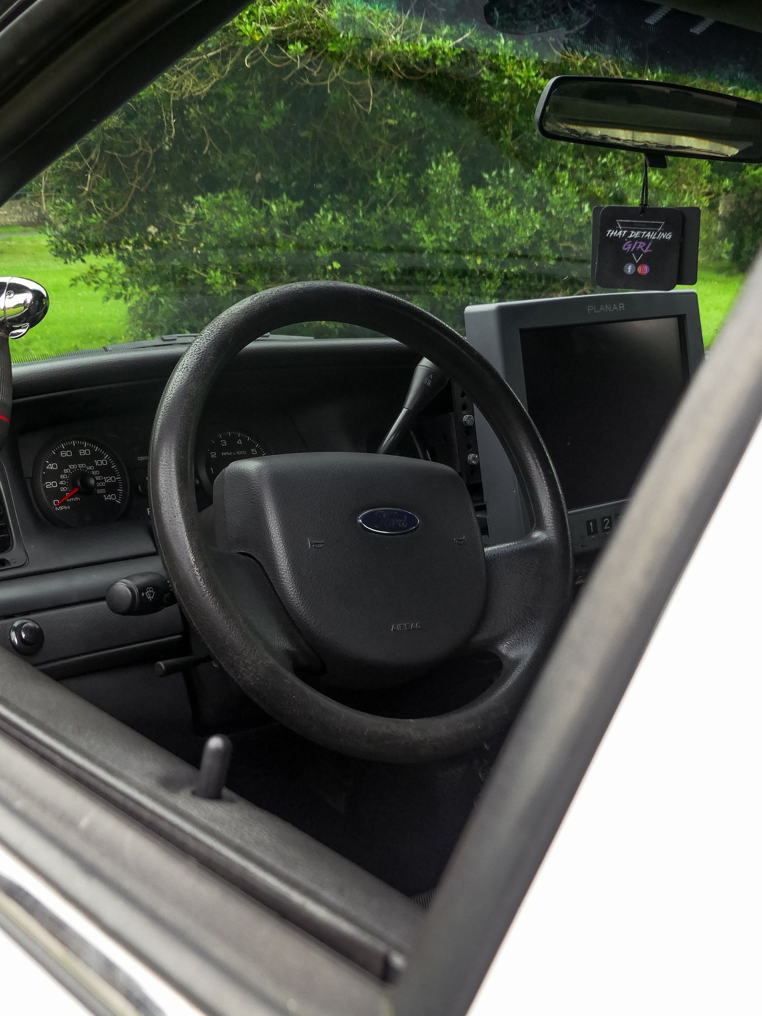 Interior view of a vehicle dashboard showing black steering wheel and instrument panel in low lighting conditions.