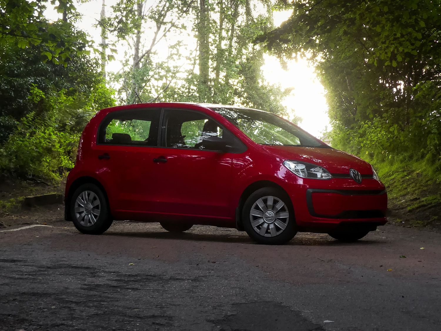 Eight connected images show a red VW photographed at sunset from different angles on a tree-lined road.